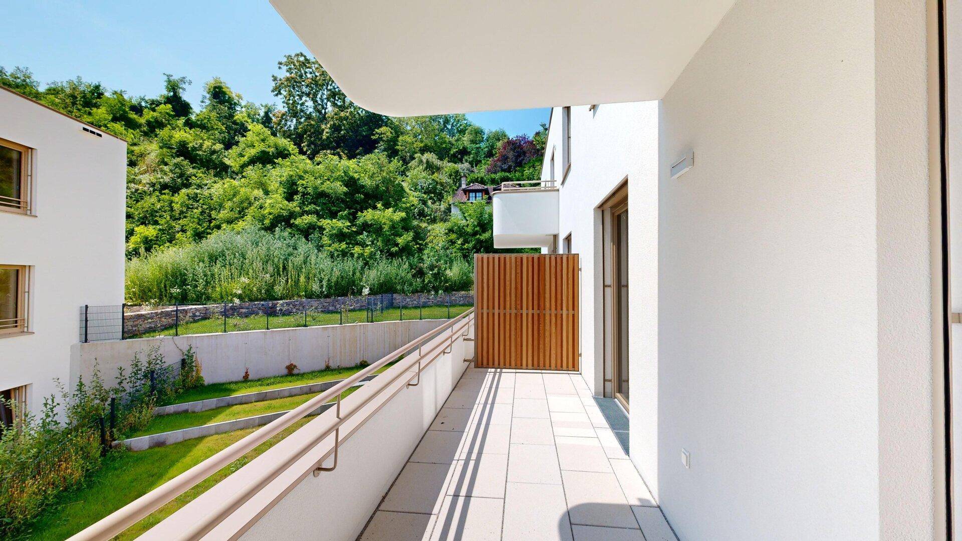 Heller Balkon mit Fliesenboden und Blick ins Grüne, umgeben von moderner Architektur.
