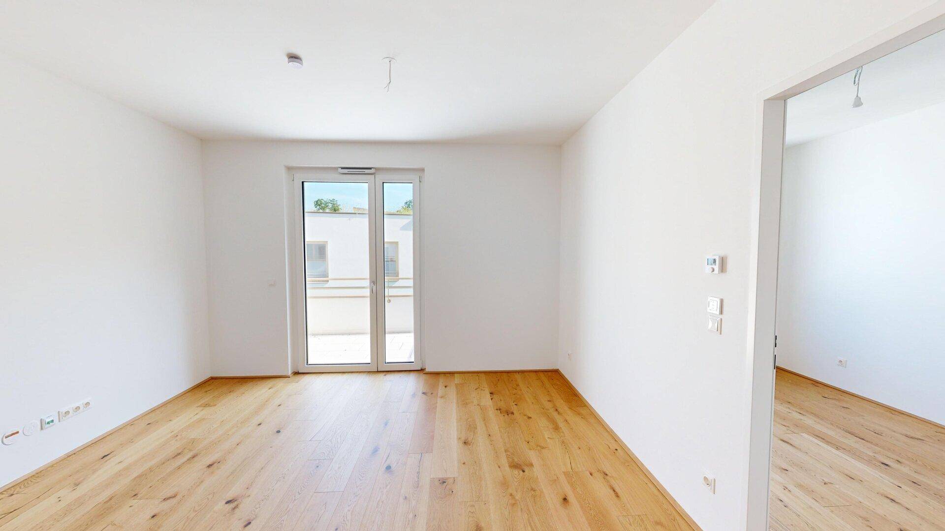 Heller, leerer Raum mit Eichenparkettboden und Zugang zu einem Balkon oder einer Terrasse.