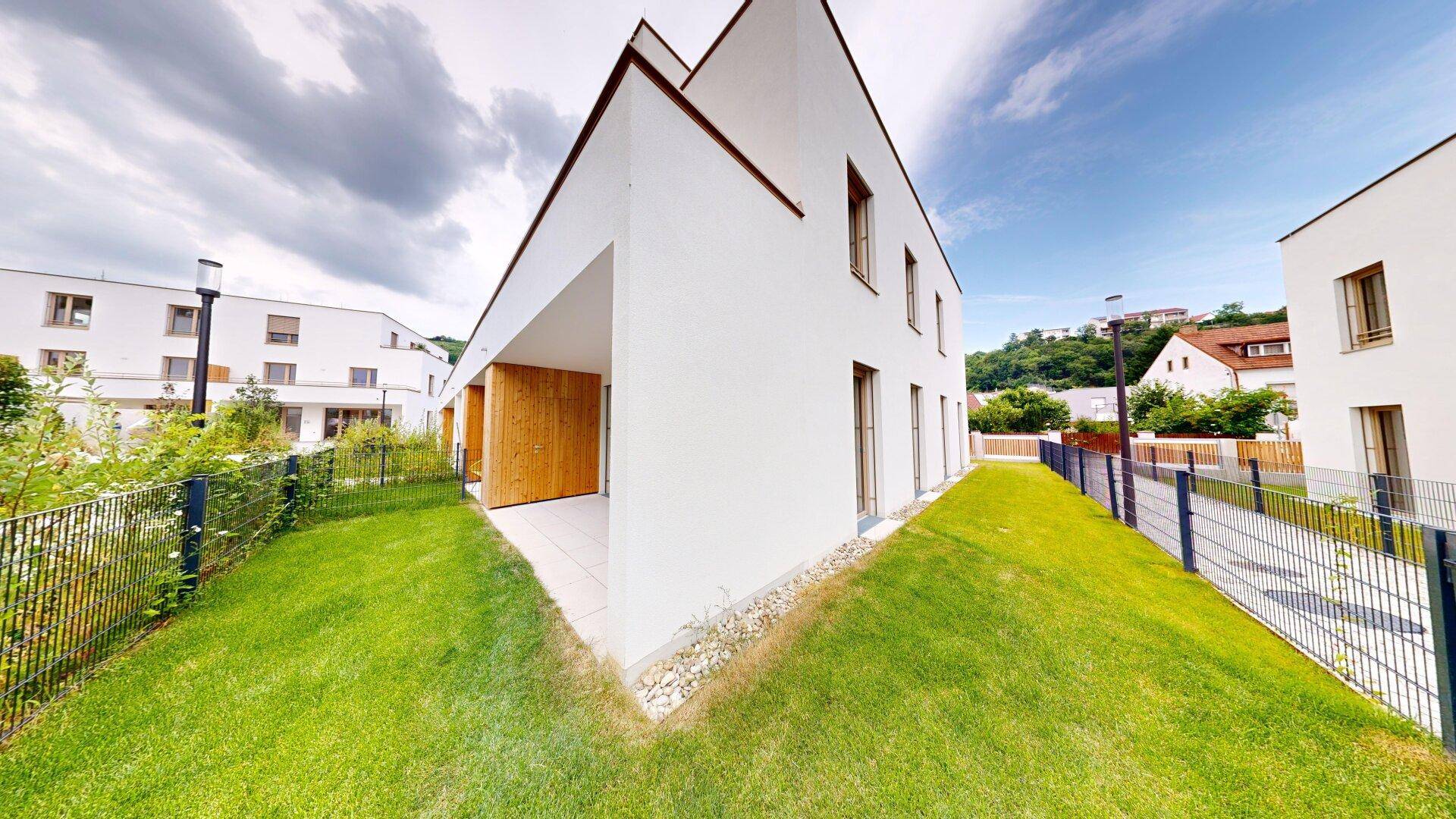 Seitenansicht eines modernen Neubaus mit weißer Fassade und gepflegtem Rasenbereich.