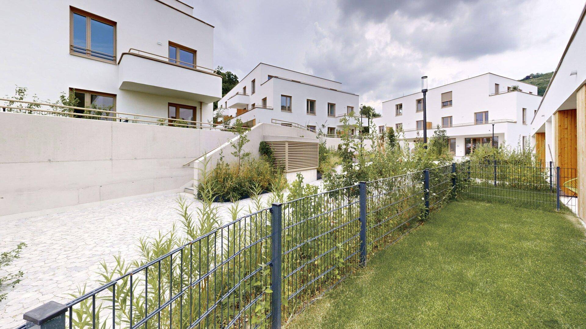 Ansicht mehrerer moderner Wohngebäude mit weißer Fassade und gepflasterten Außenbereichen.