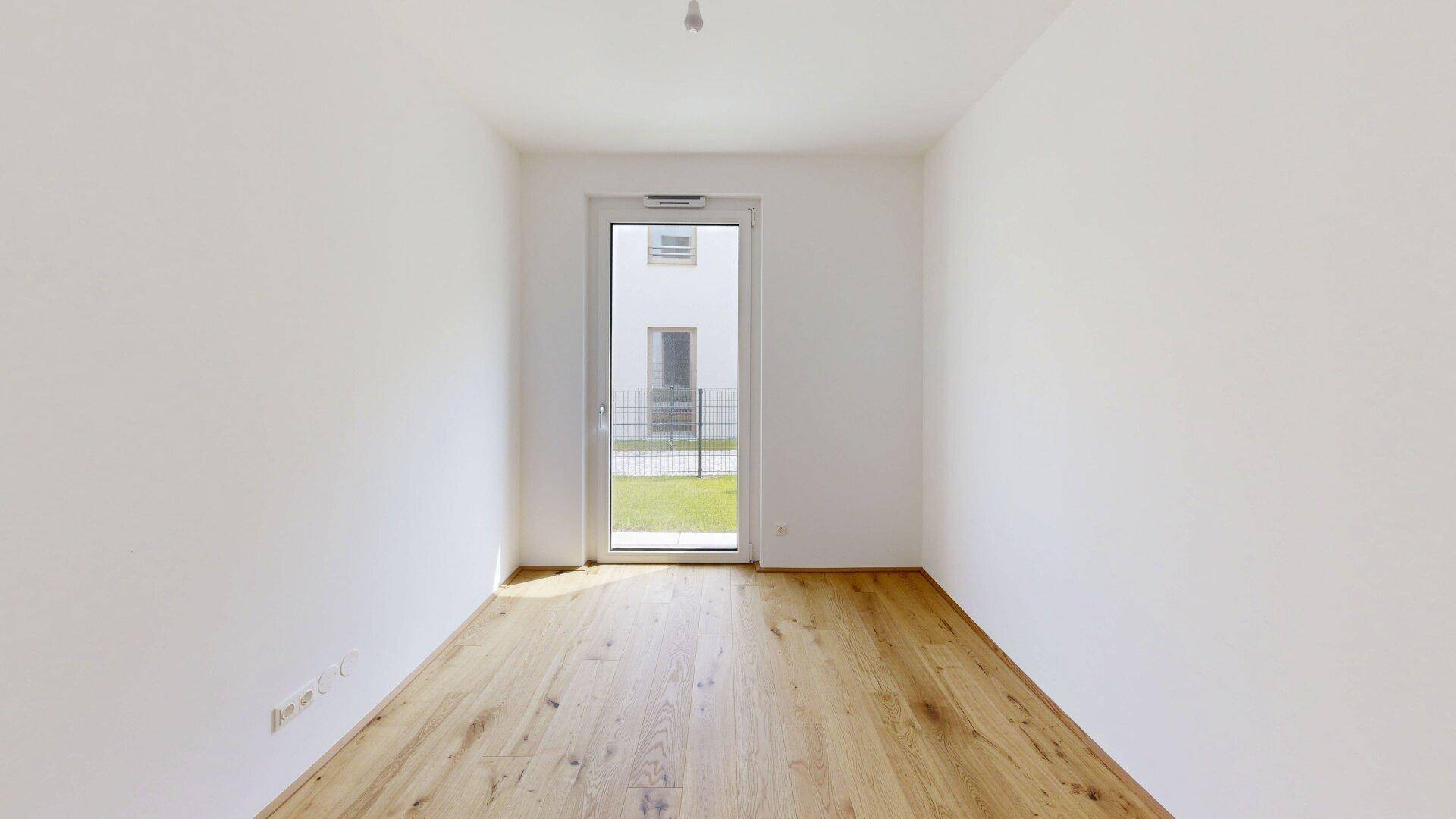Leeres Zimmer mit Holzboden und einer Tür, die direkten Zugang zum Außenbereich ermöglicht.