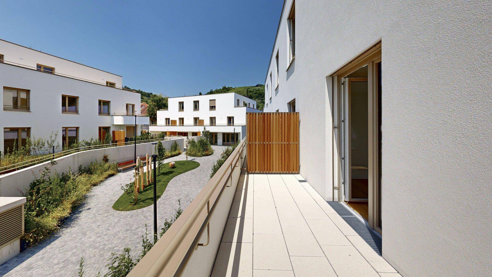 Heller Balkon mit Fliesenboden und Blick auf den begrünten Innenhof der modernen Wohnanlage.