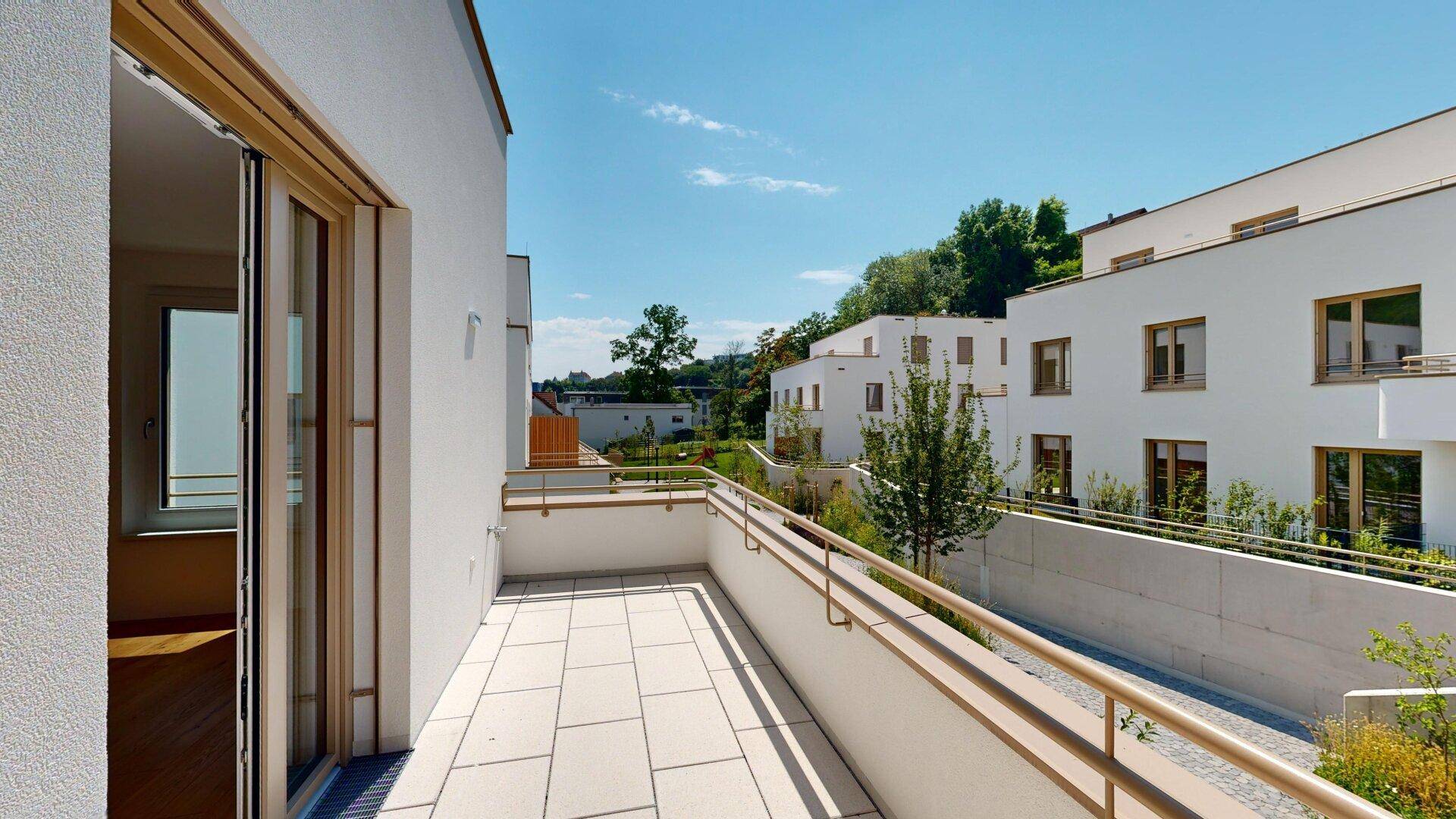 Geräumiger Balkon mit Fliesenboden und Blick auf die umliegende grüne Landschaft und Wohngebäude.