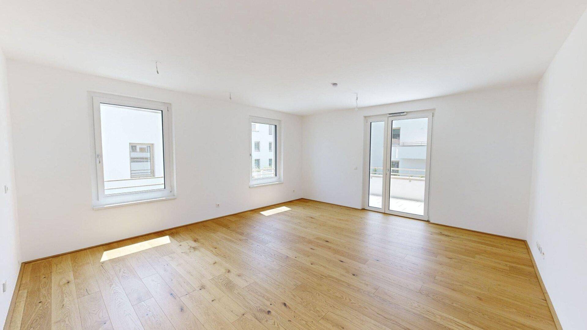 Helles, leeres Wohnzimmer mit Eichenparkettboden und Zugang zu einem Balkon.