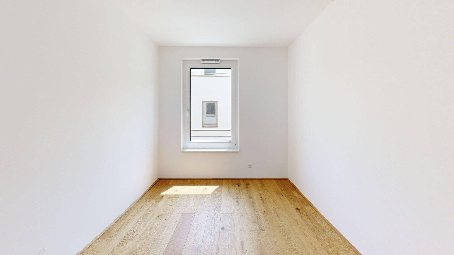 Helles Zimmer mit Eichenparkettboden und einem Fenster, das viel Tageslicht hereinlässt.
