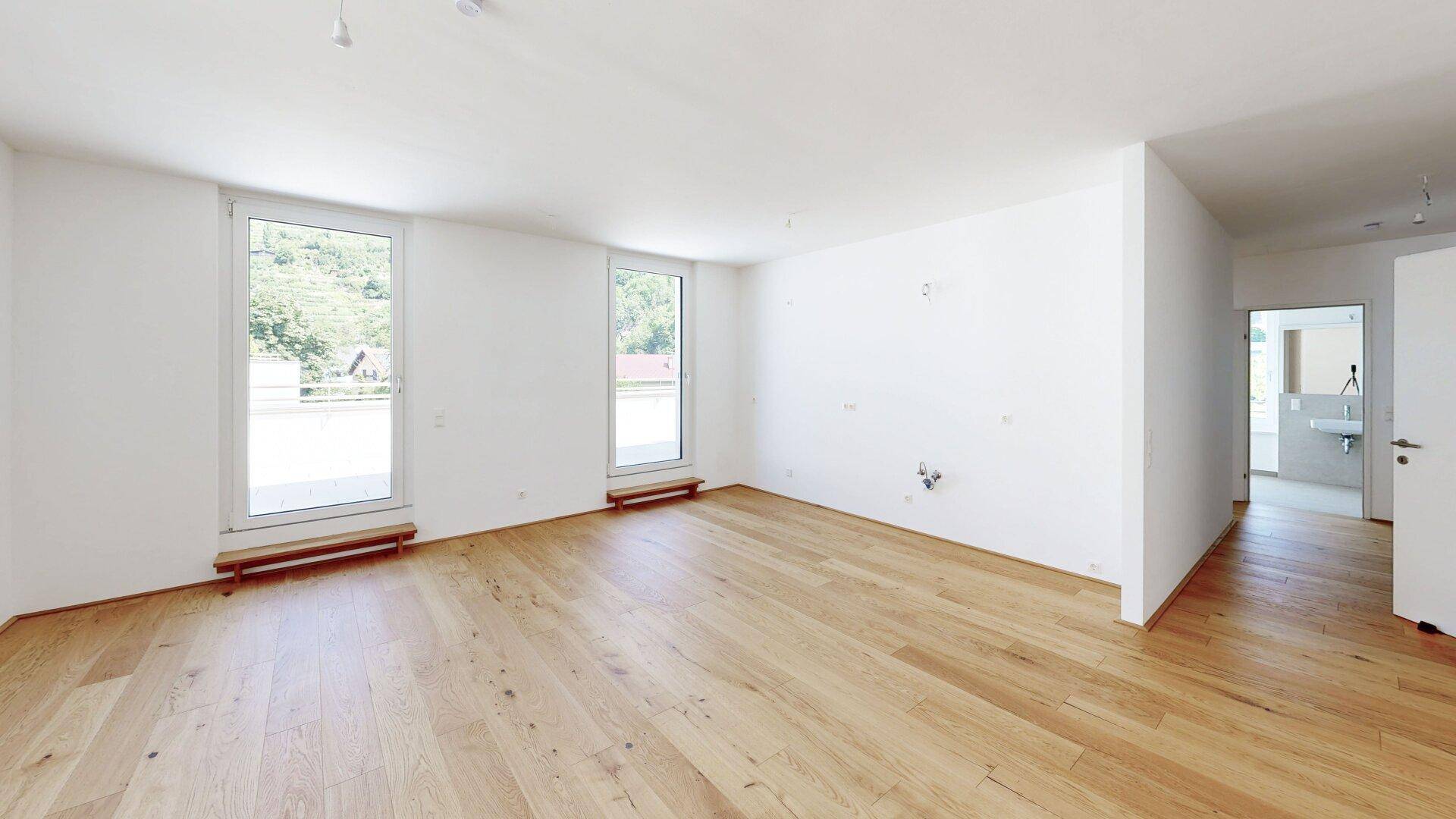 Geräumiges, helles Zimmer mit Holzboden und Zugang zu einem weiteren Bereich, ideal für Wohnen.