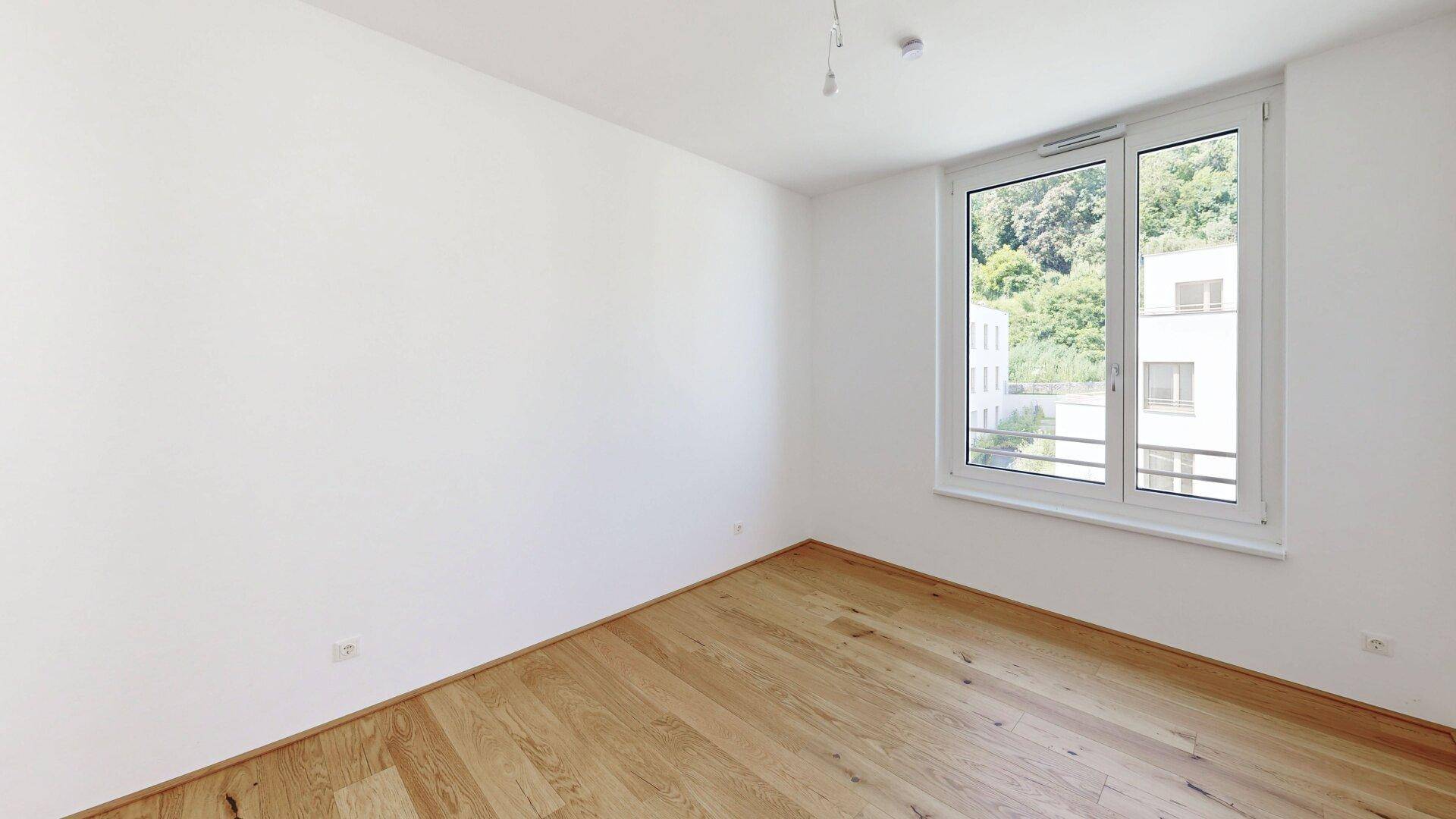 Helles Schlafzimmer mit Holzboden und Blick ins Grüne, ideal für erholsame Nächte.