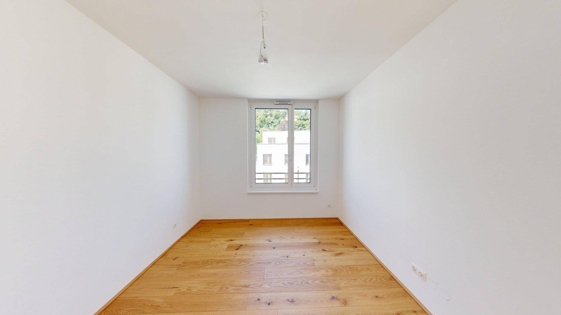 Ruhiges Schlafzimmer mit Holzboden und einem Fenster, das viel Tageslicht hereinlässt.