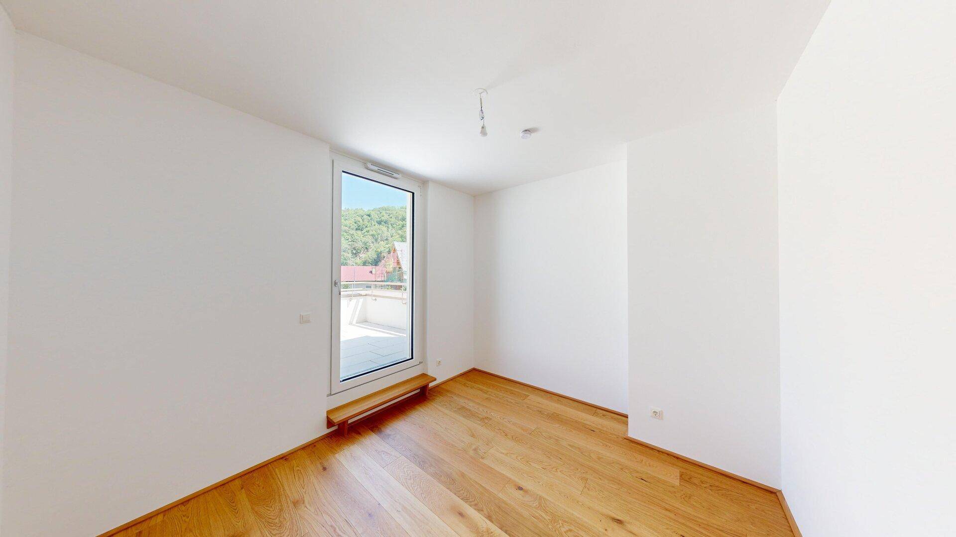 Geräumiges Zimmer mit Holzboden und großer Fenstertür, die zu einem Außenbereich führt.