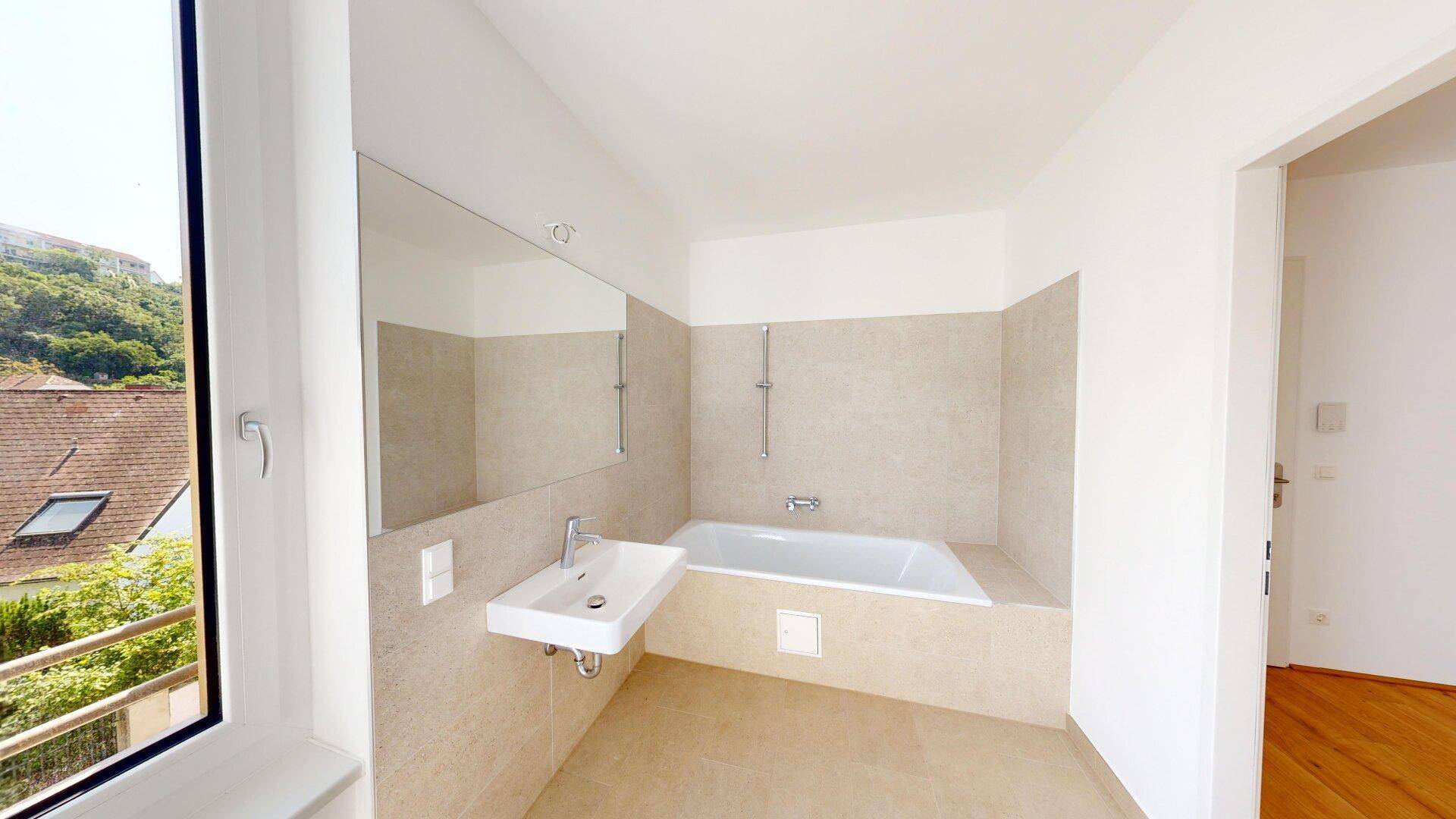 Modernes Badezimmer mit Badewanne, Einzelwaschbecken und hellen Fliesen, mit Fenster.