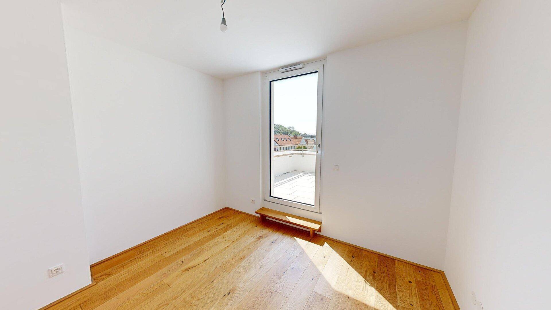 Helles Zimmer mit Holzboden und Zugang zu einem Außenbereich, ideal als Schlaf- oder Arbeitszimmer.