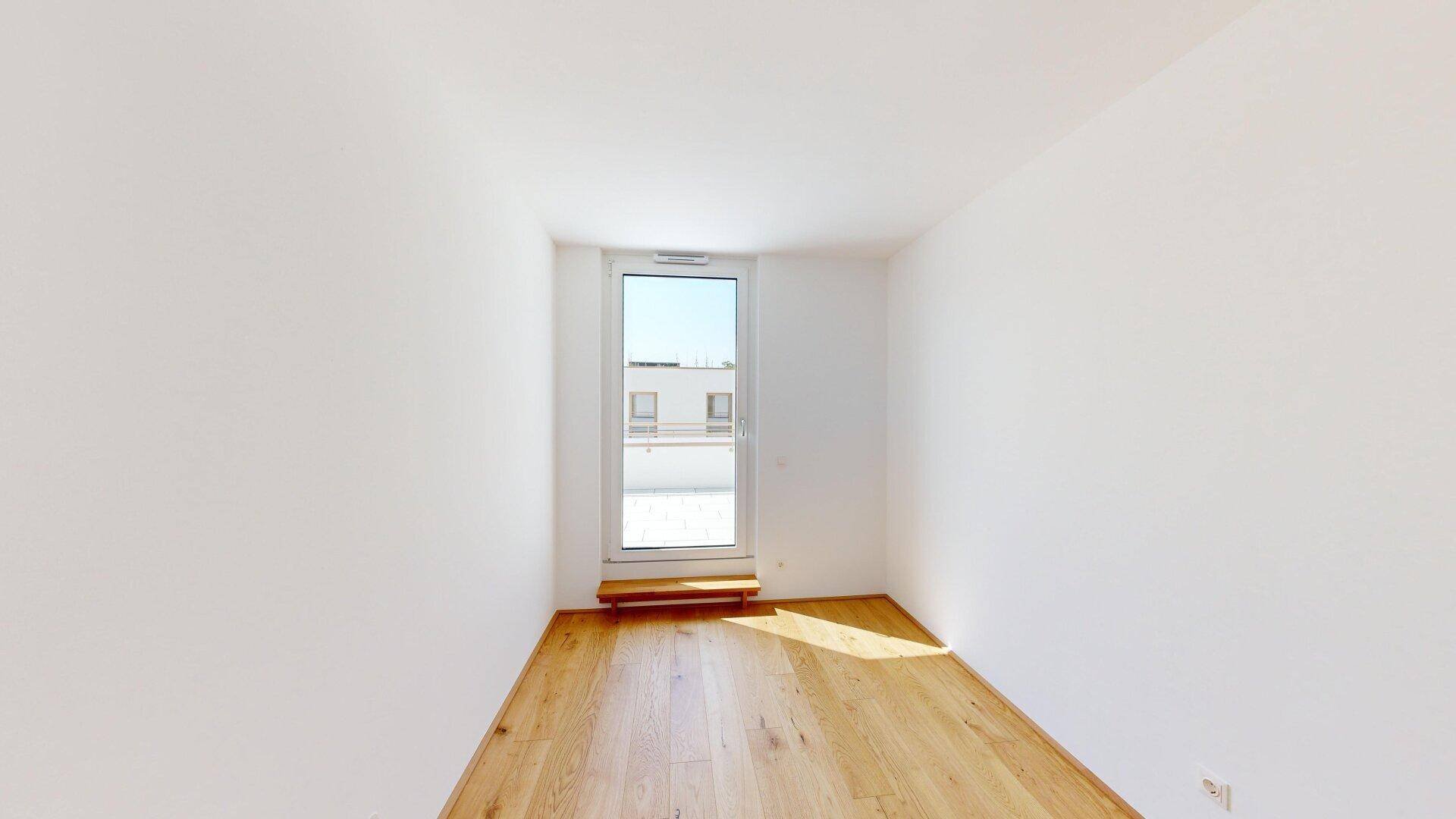 Lichtdurchflutetes Zimmer mit Parkettboden und bodentiefem Fenster, das den Raum erhellt.