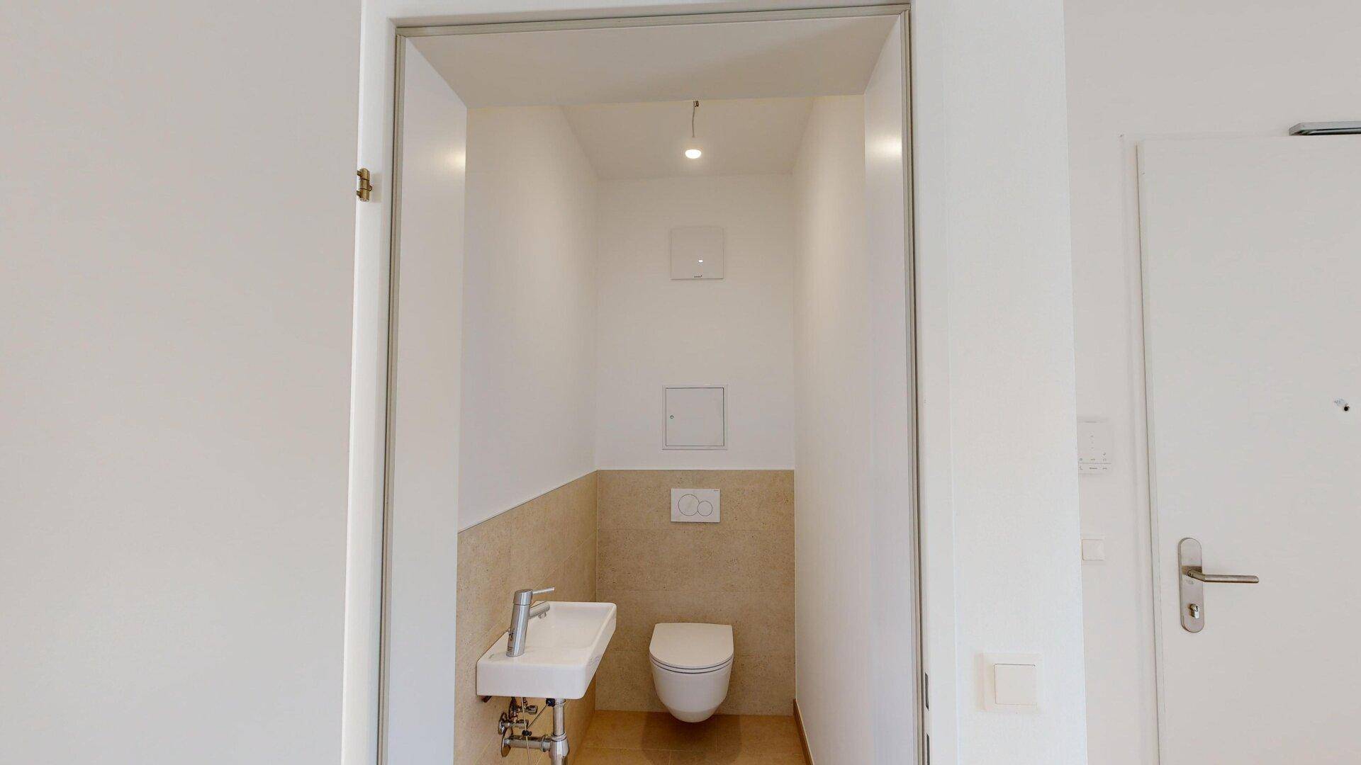 Praktisches Gäste-WC mit wandhängender Toilette und kleinem Handwaschbecken, halb gefliest.