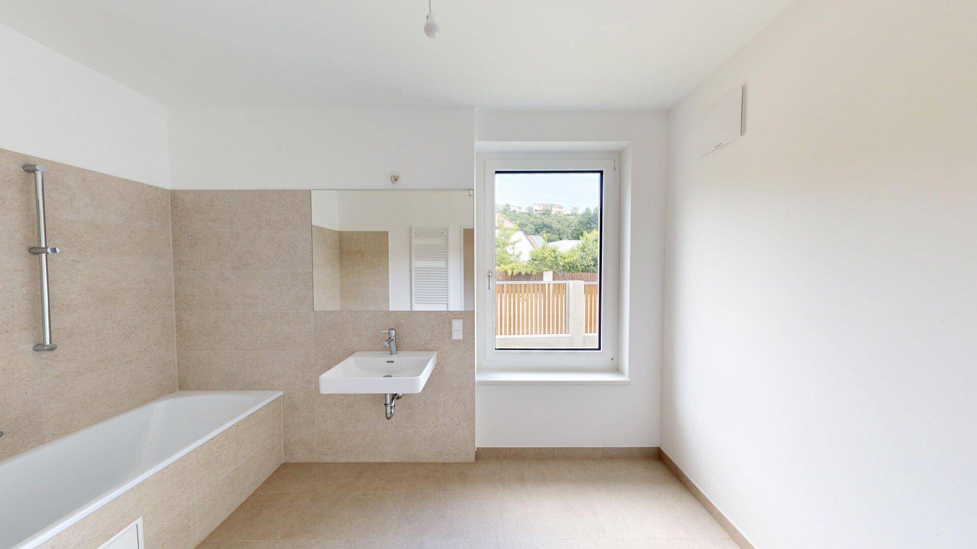 Modernes Badezimmer mit Badewanne, Waschbecken und Fenster, in hellen Beigetönen gehalten.
