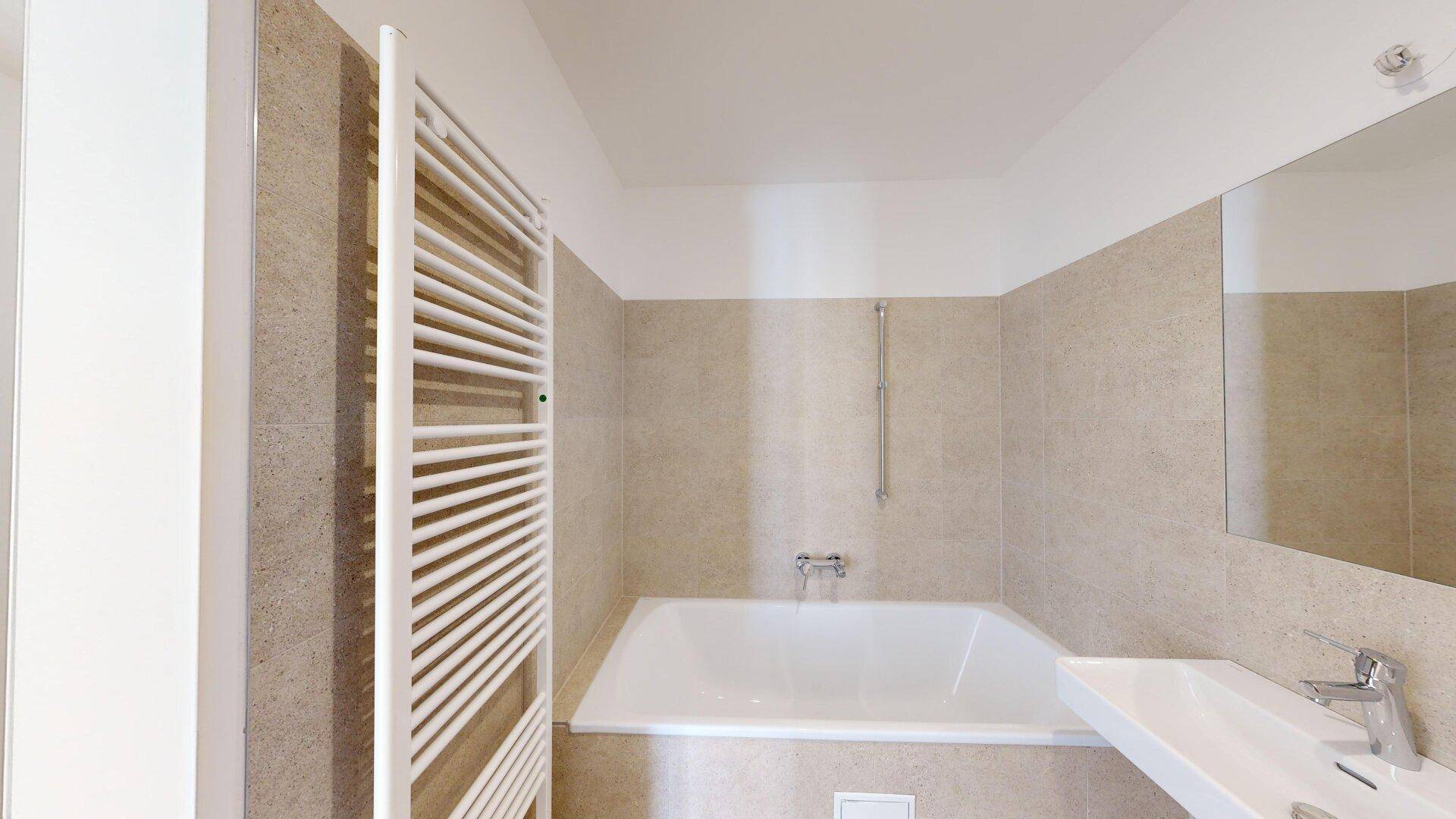 Modernes Badezimmer mit beigefarbenen Fliesen, Badewanne und beheiztem Handtuchhalter.