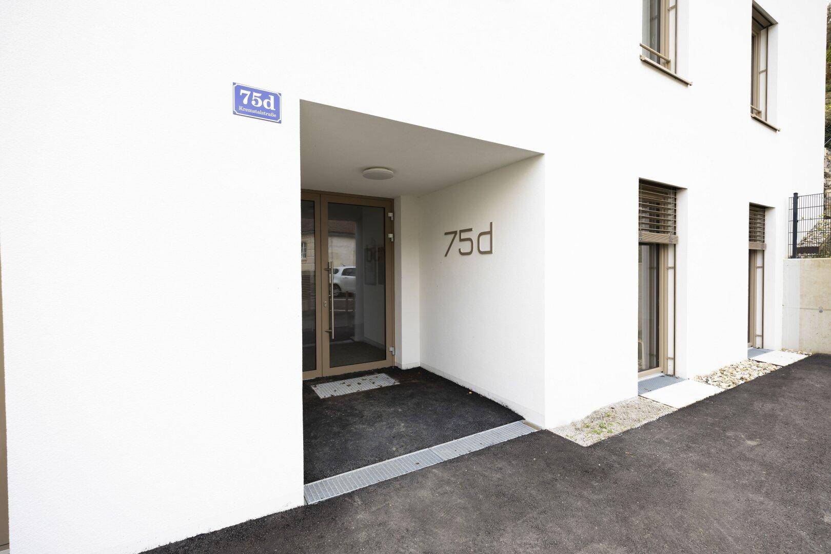 Moderner Eingangsbereich eines Wohngebäudes mit weißer Fassade und Glasportal.