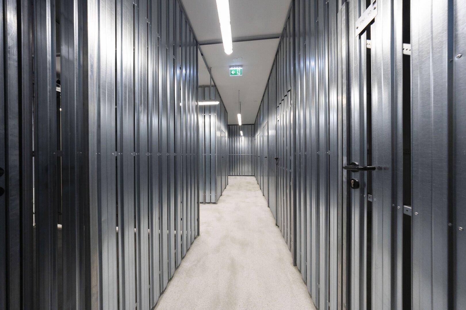 Langer Gang im Keller mit zahlreichen abschließbaren Abstellräumen aus Metall.