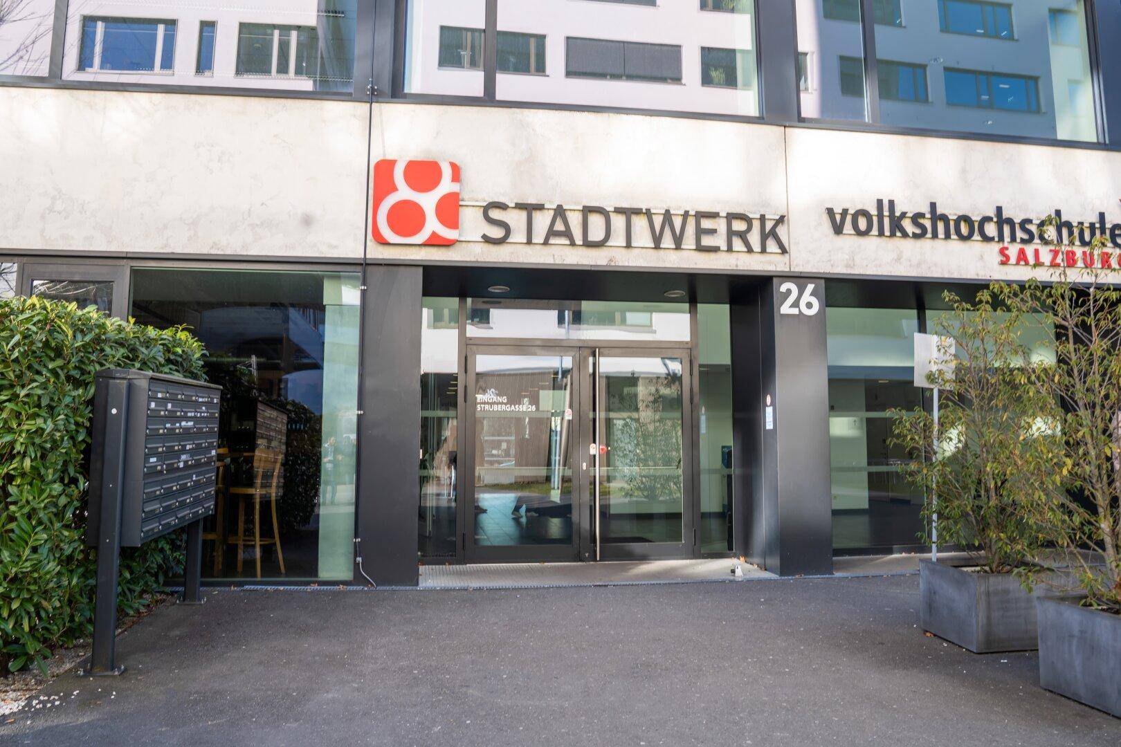 Eingangsbereich eines modernen Gebäudes mit Glasfassade und Beschilderung für "STADTWERK" und "Volkshochschule".