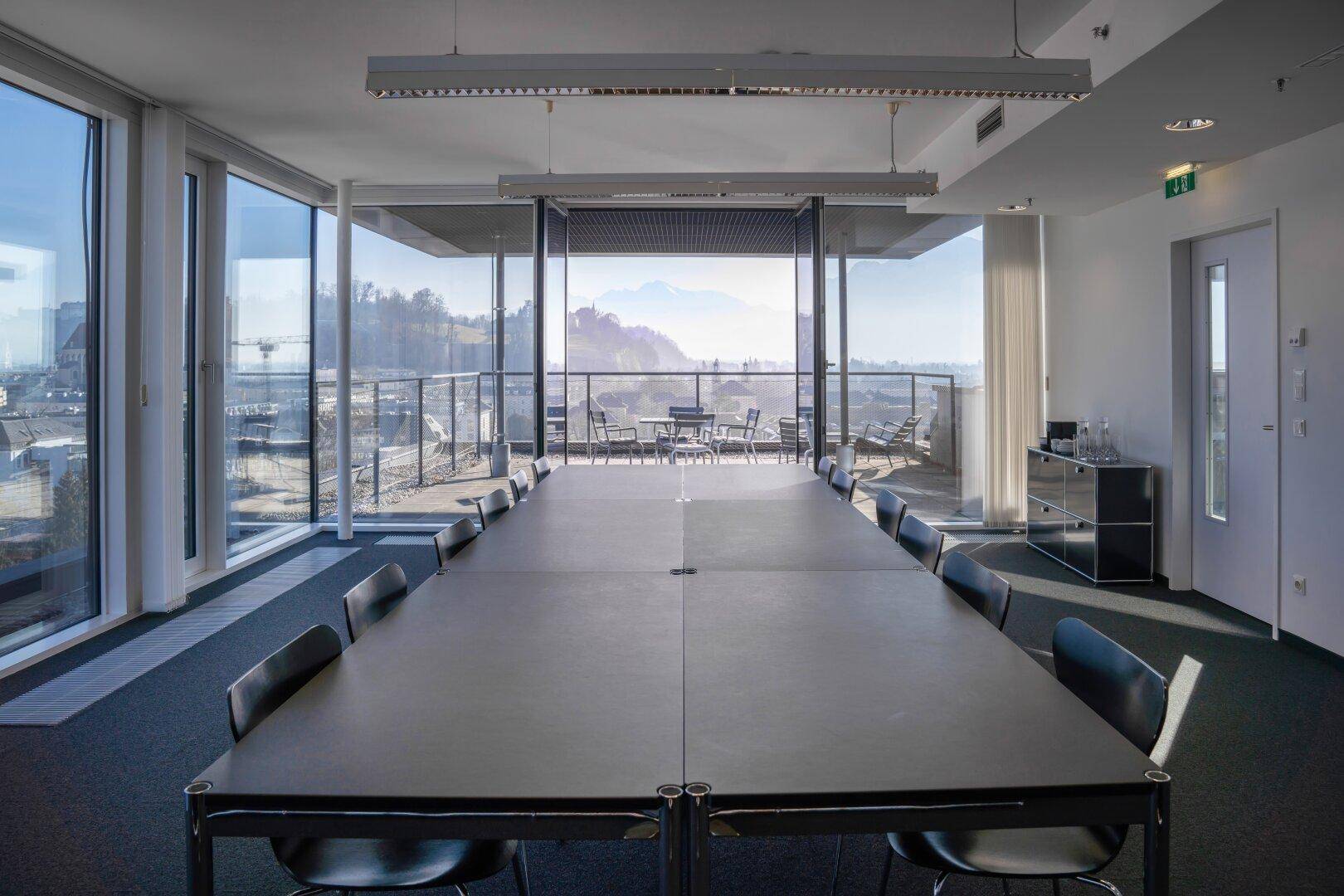 Großer Konferenztisch in einem modernen Raum mit weitem Blick auf die Berge und die Stadt durch die Glasfront.