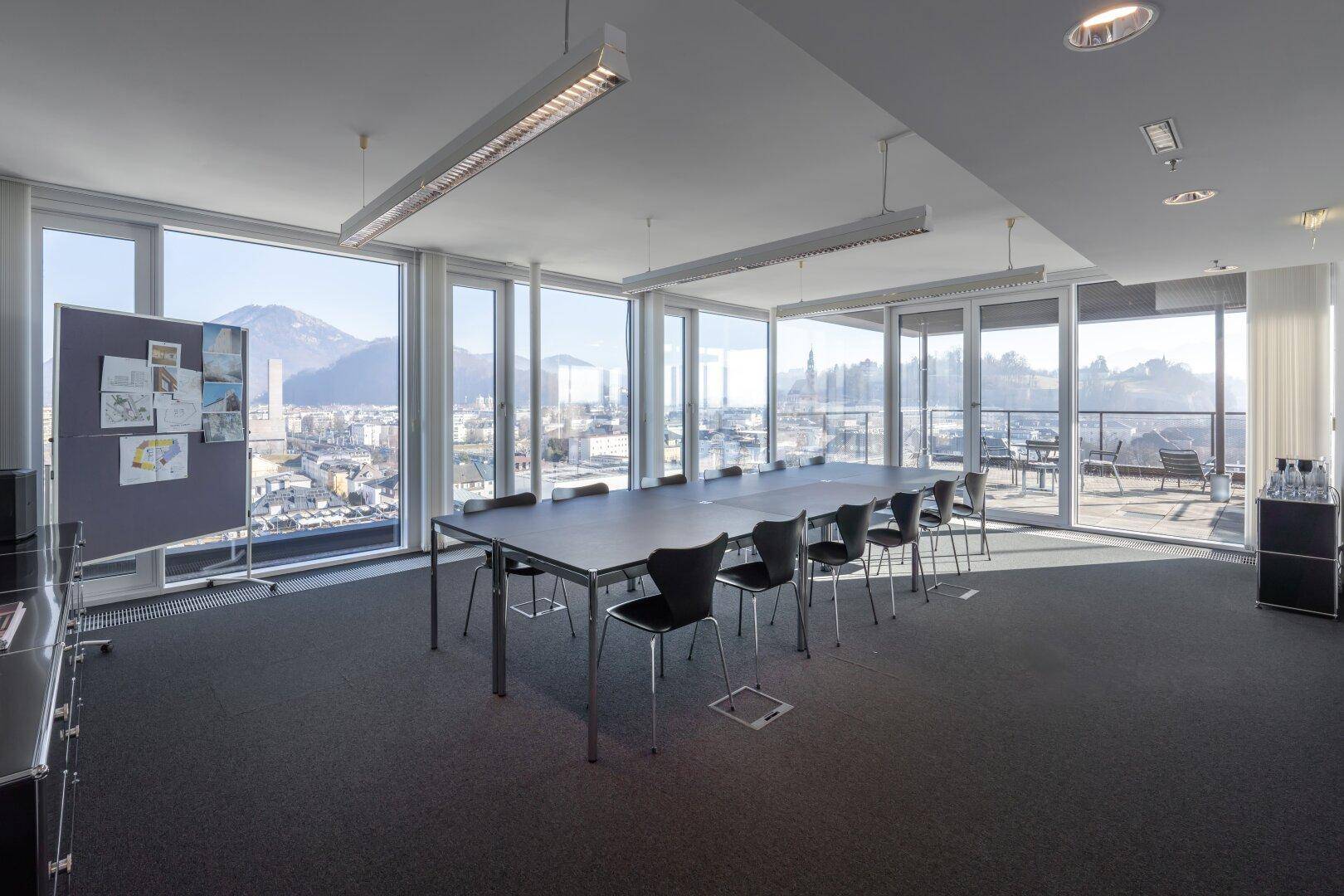 Heller Konferenzraum mit langer Tafel, vielen Stühlen und raumhohen Fenstern mit Stadt- und Bergblick.