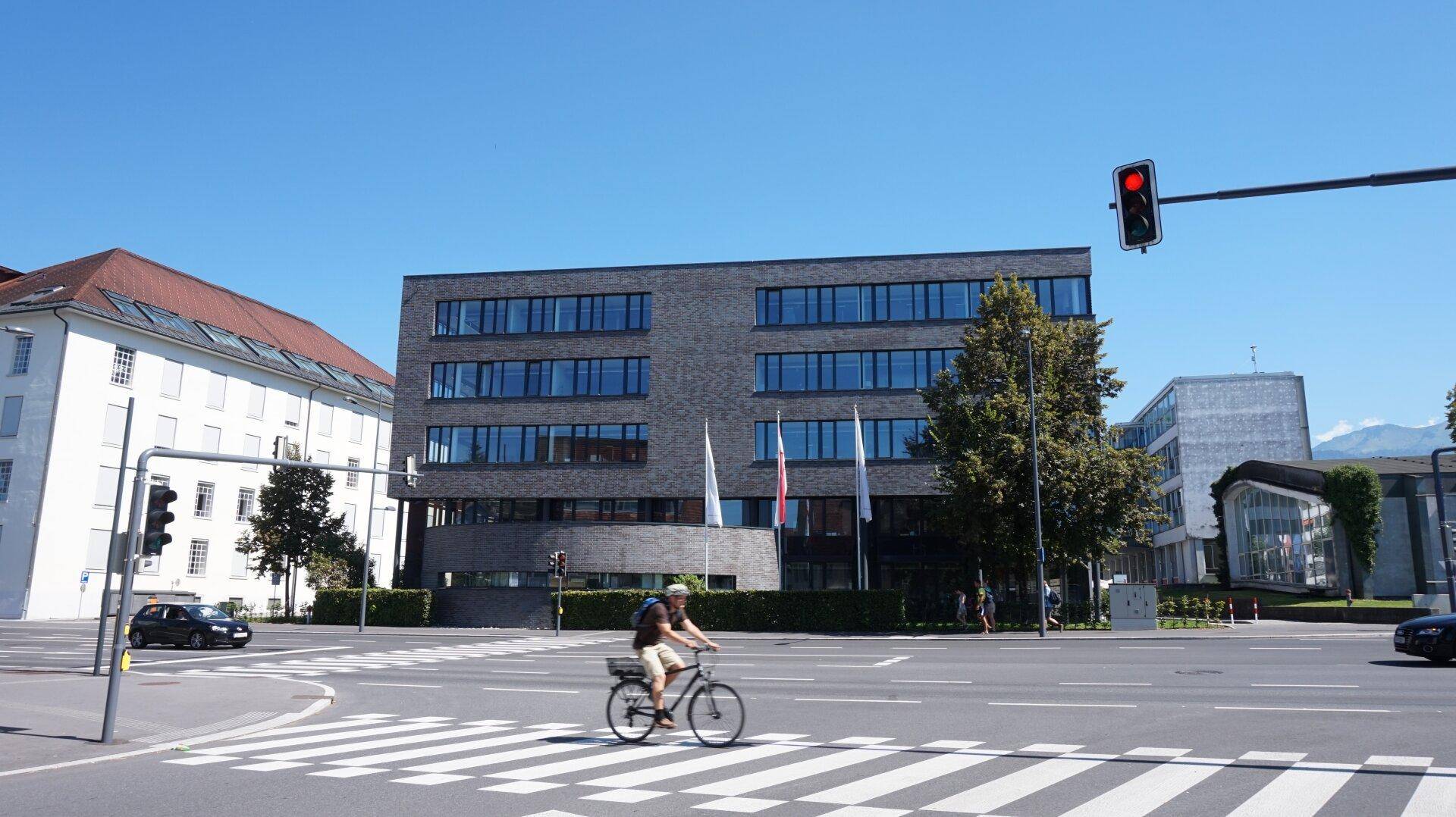 Modernes Gebäude an einer Kreuzung mit klarem blauen Himmel und Passanten.
