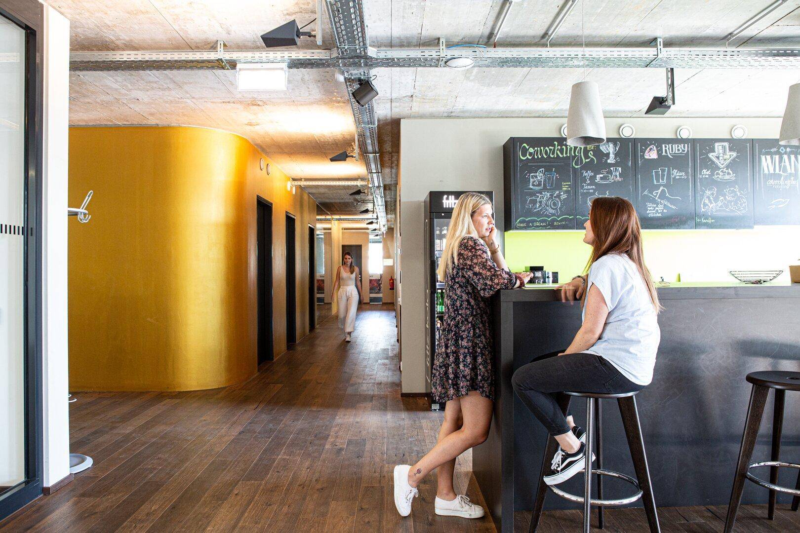 Moderner Loungebereich mit Bar, Holzboden und gelb gestrichenen Wänden in einem Bürogebäude.