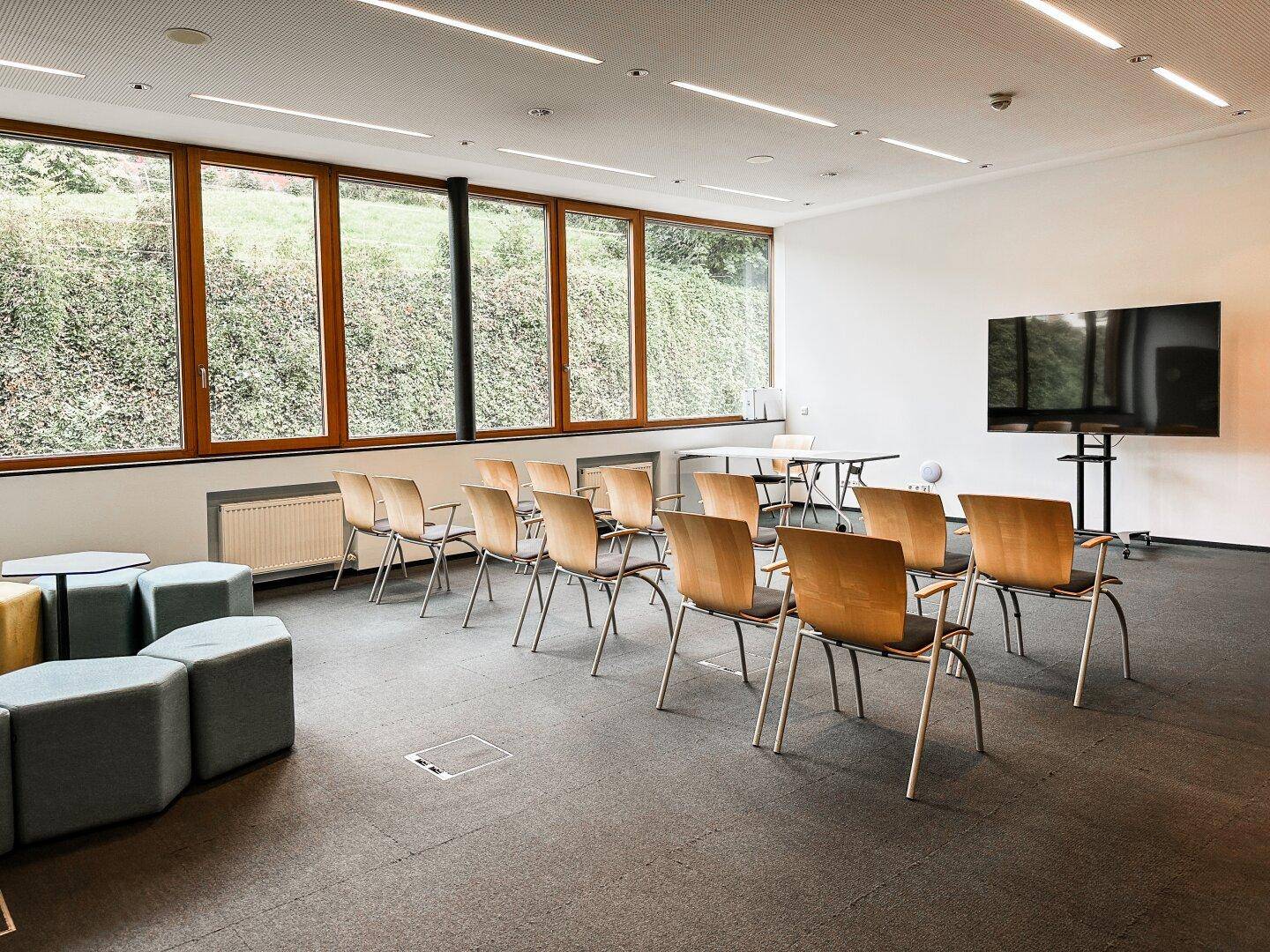 Großer Konferenzraum mit vielen Stühlen, einem Bildschirm und weitem Blick ins Grüne durch die Fenster.