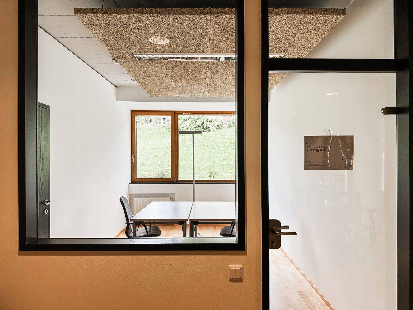 Ein modernes Büro mit Glaswänden, Holzboden und einem weiten Blick auf die umliegende Natur.