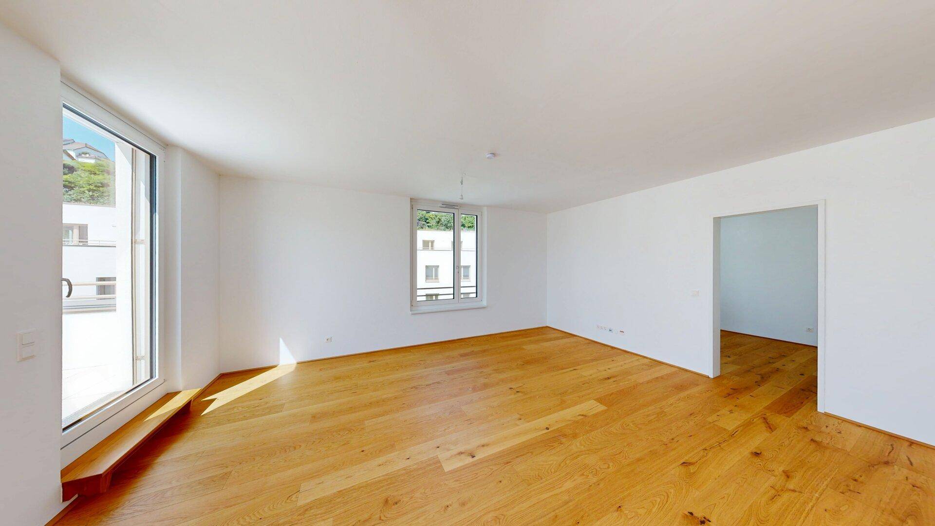 Geräumiger, unmöblierter Raum mit hellem Holzfußboden und großen Fenstern für viel Helligkeit.