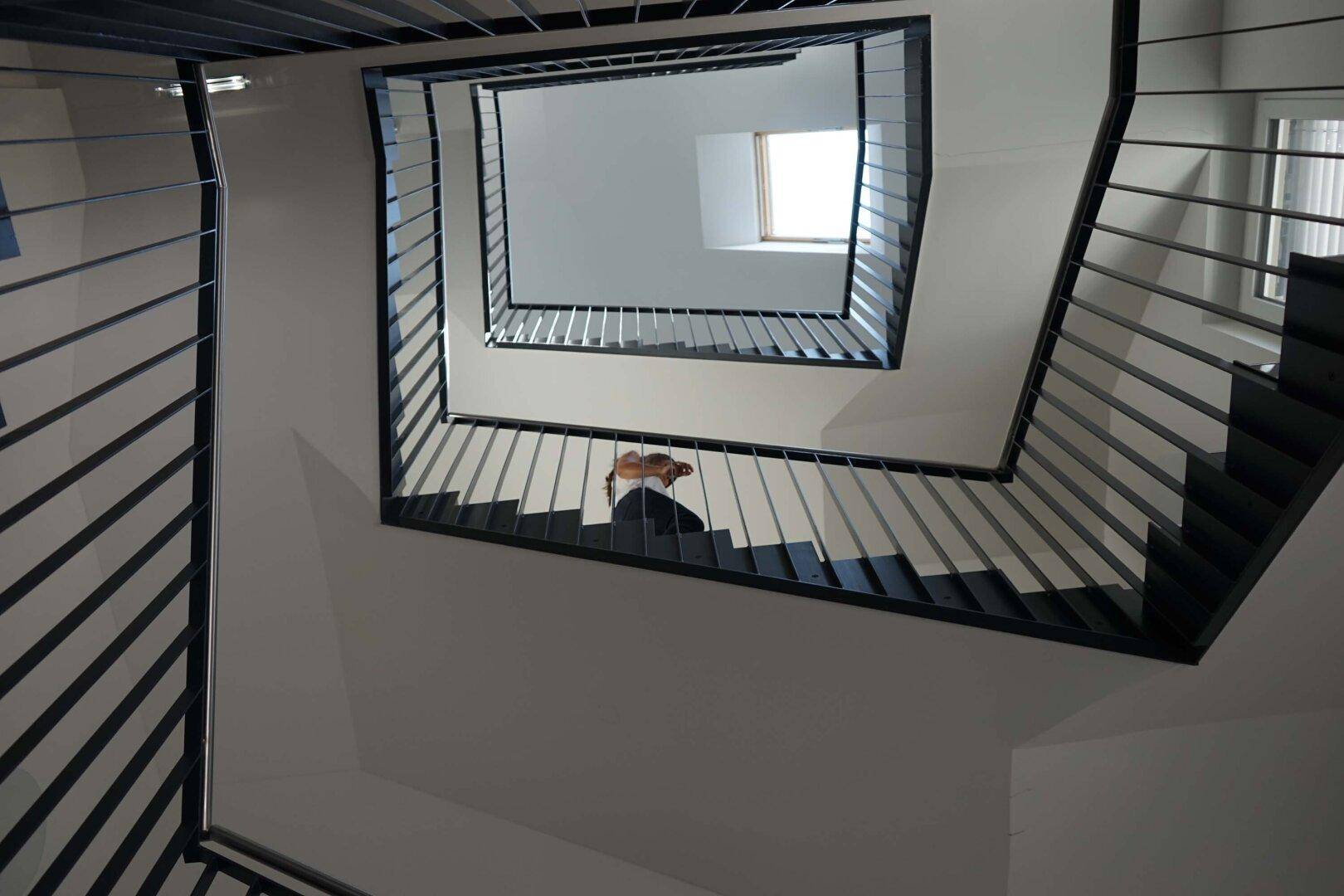 Modernes Treppenhaus mit Metallgeländer und Oberlicht, von oben fotografiert.