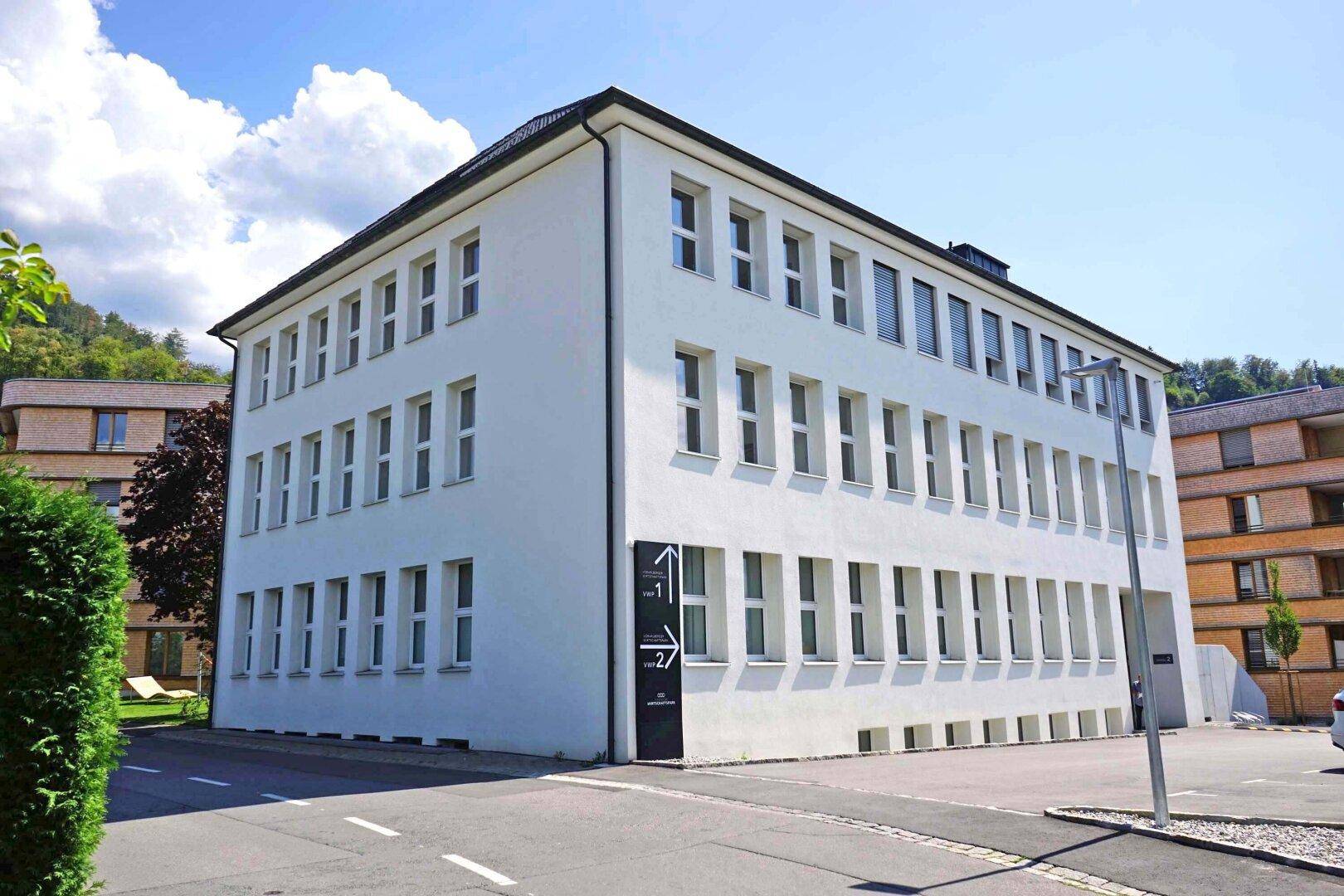 Modernes, weißes Bürogebäude mit vielen Fenstern und klarem Himmel.