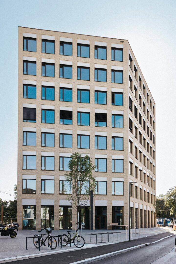 Hohes, modernes Gebäude mit vielen Fenstern und einer hellen Fassade an einem sonnigen Tag.