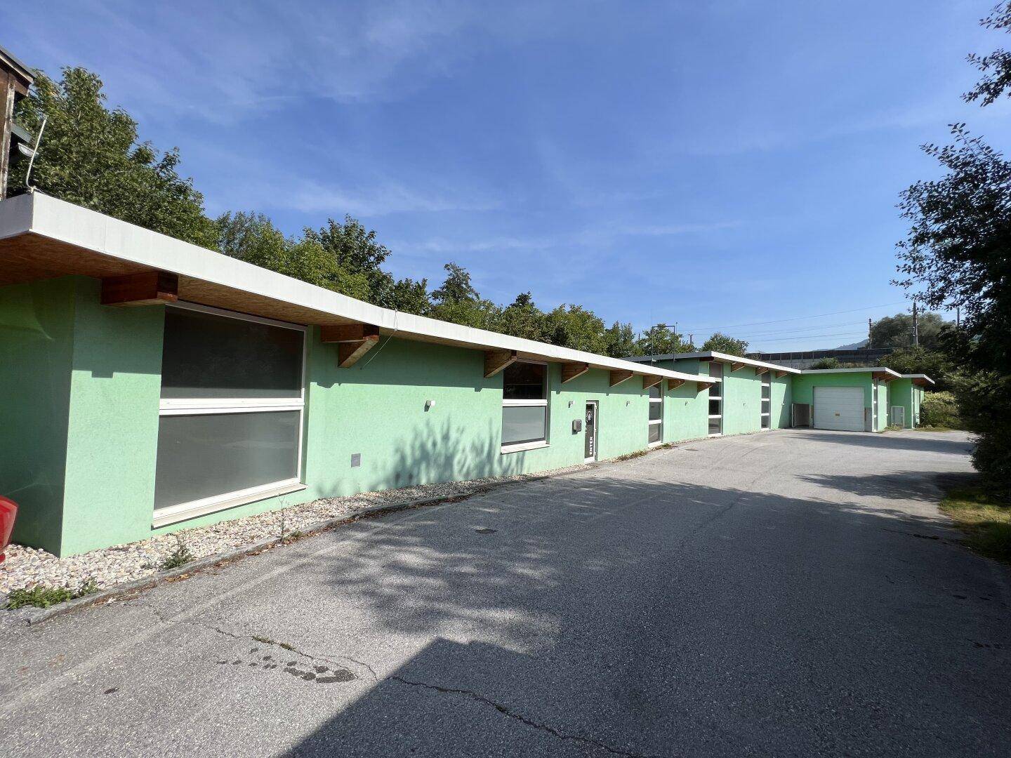 Lange Reihe von Gebäuden mit grüner Fassade, großen Fenstern und Holzdachüberstand.