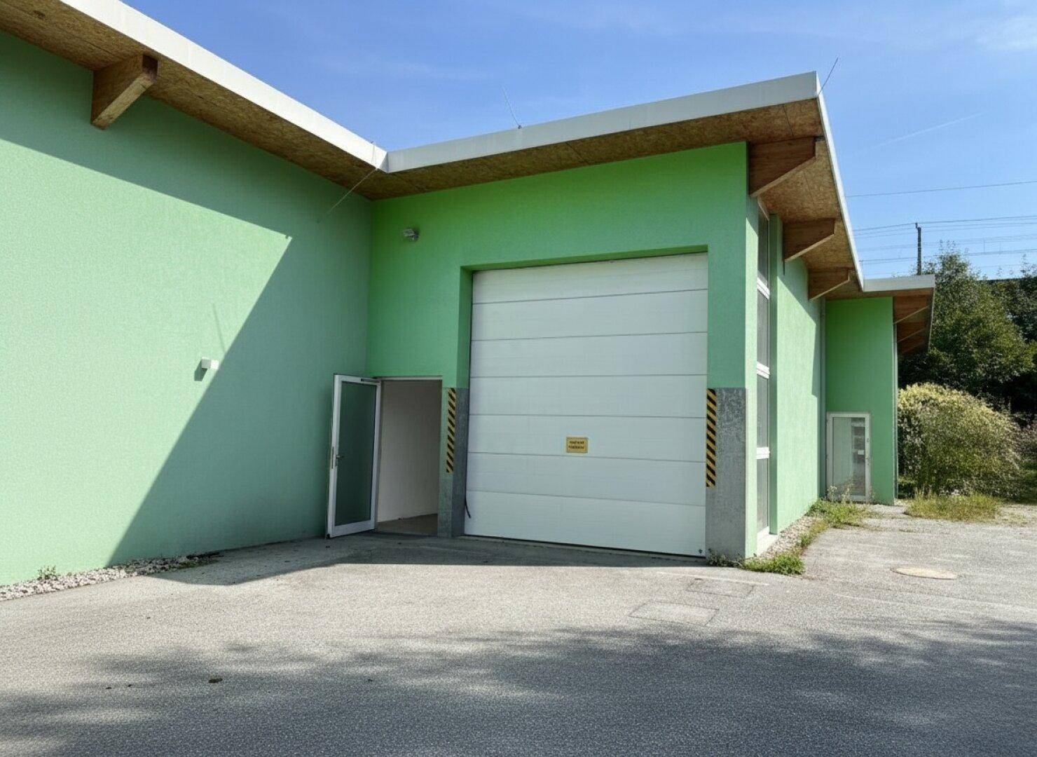 Gebäudeecke mit grün gestrichener Fassade, großem Rolltor und Eingangstür.