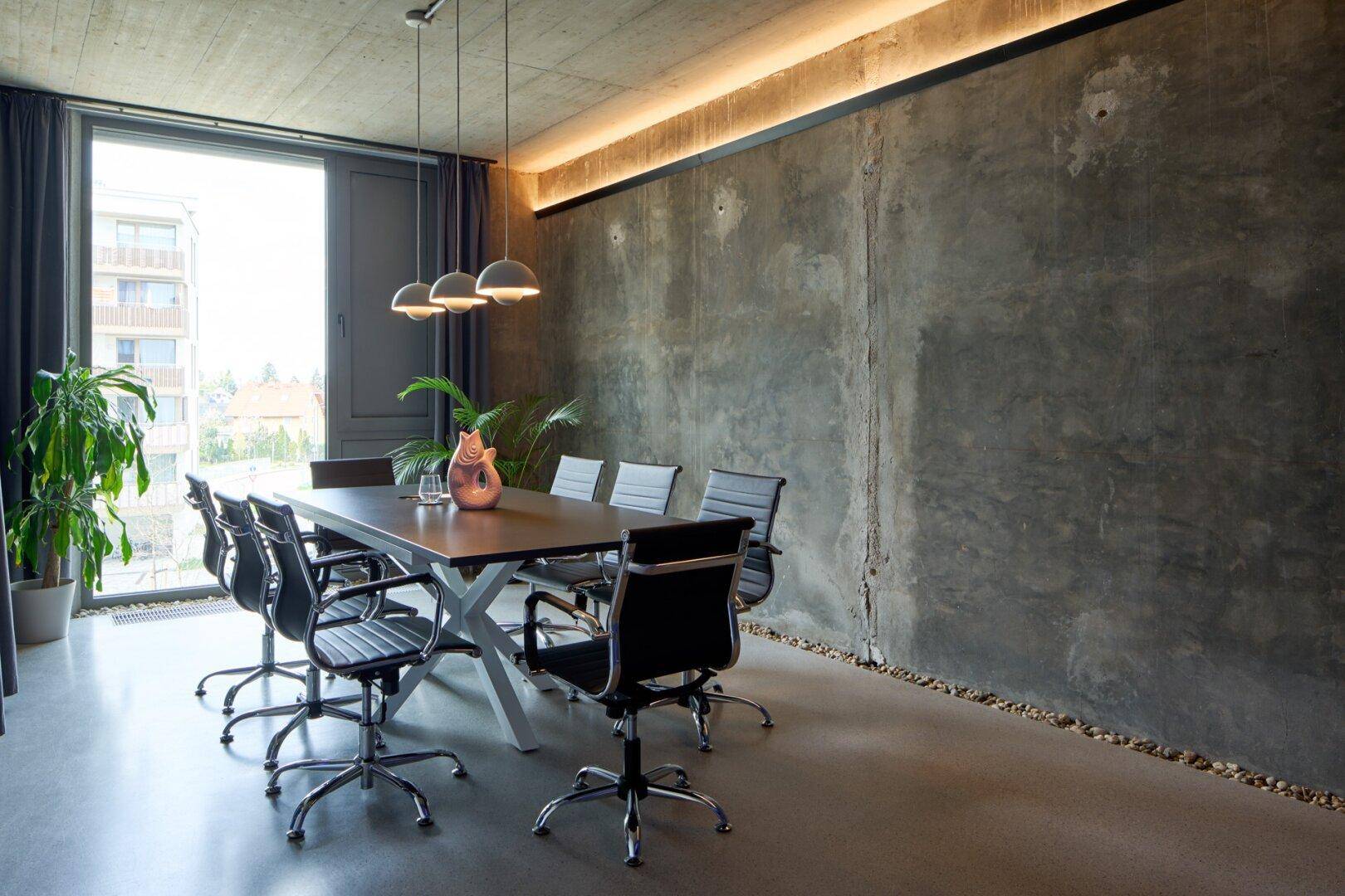Konferenzraum mit großem Tisch, modernen Stühlen und einer Wand aus Sichtbeton.