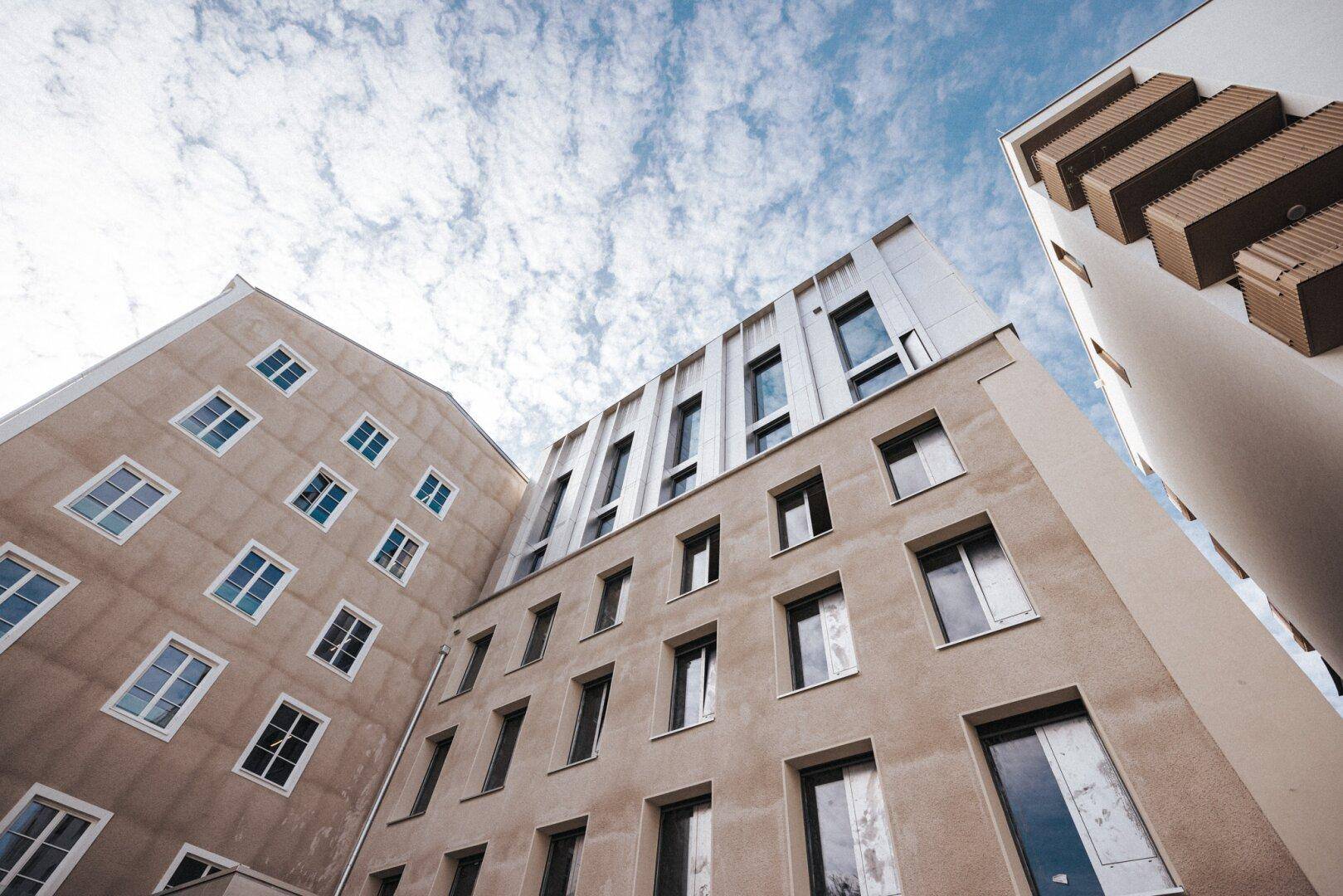 Ansicht von unten auf die Fassaden mehrerer Gebäude mit unterschiedlichen Fensterformen.