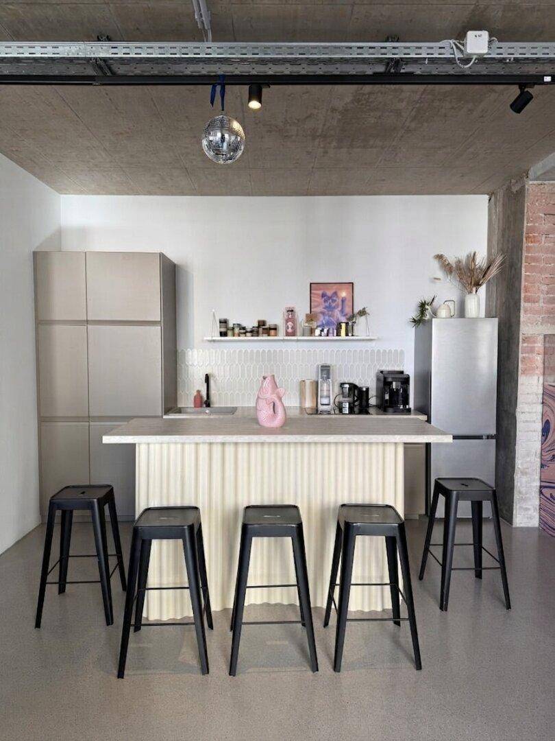 Moderne Küchenzeile mit Kochinsel, Barhockern und einem Kühlschrank in Edelstahloptik.
