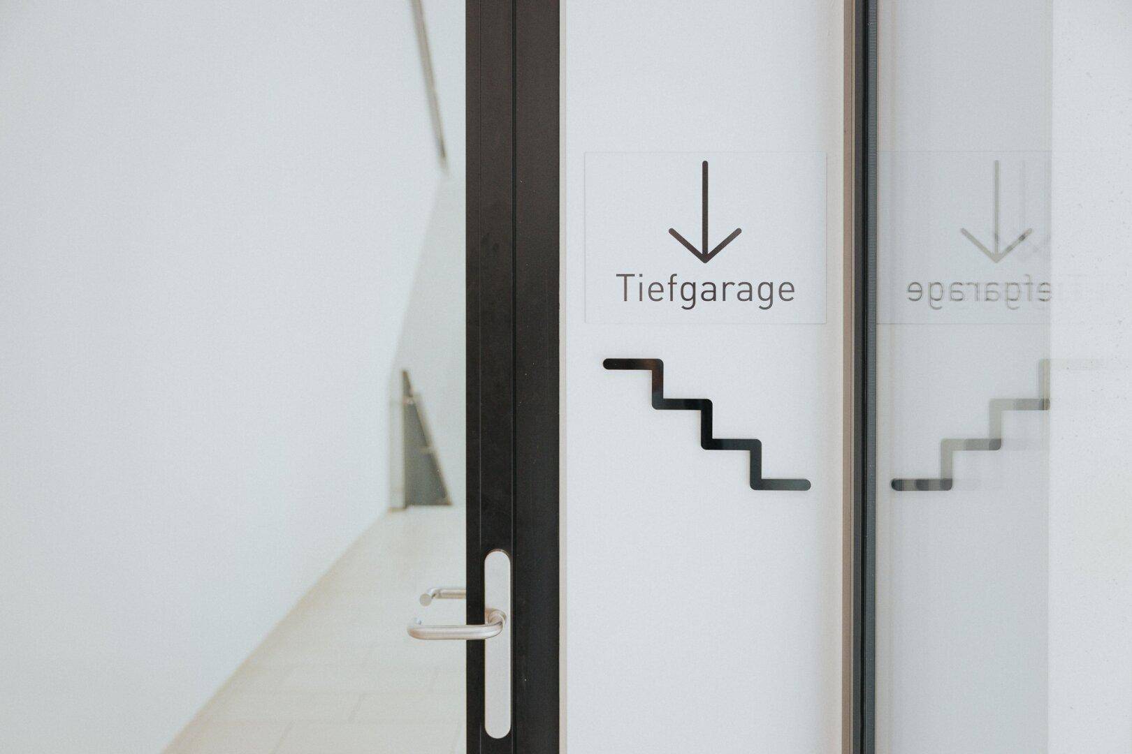 Glastür mit Beschriftung 'Tiefgarage' und einem Pfeil, der den Weg nach unten weist.