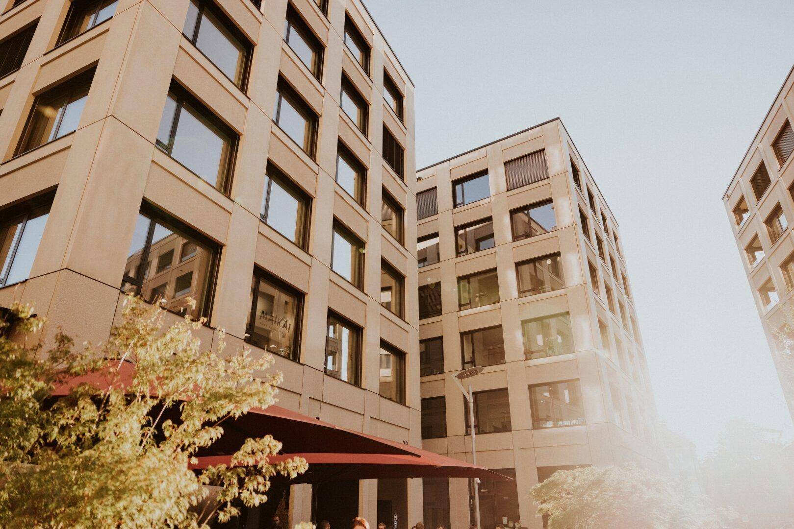 Mehrere moderne Gebäude mit vielen Fenstern, beleuchtet von der strahlenden Sonne.