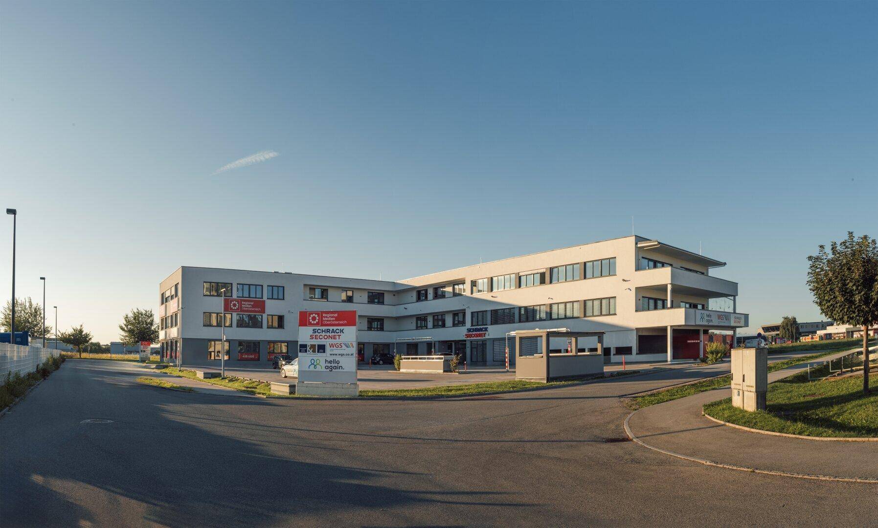 Weitläufiges modernes Bürogebäude mit mehreren Etagen und einem großen Parkplatz im Freien.