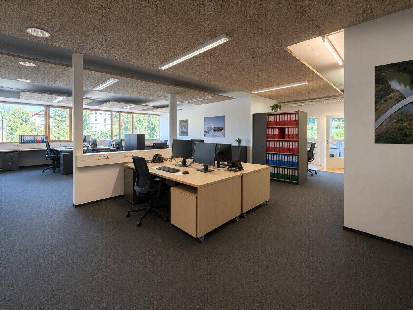 Offenes Büro mit mehreren Arbeitsplätzen, Akustikdeckenplatten und Blick auf die Umgebung.