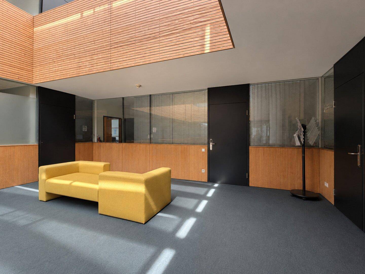 Moderner Empfangsbereich mit gelbem Sofa, Holzverkleidung und Teppichboden.