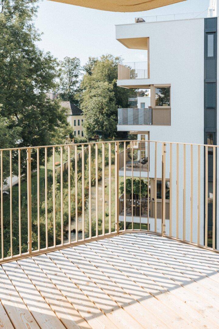 Geräumiger Balkon mit Holzboden und modernem Geländer, umgeben von viel Grün.