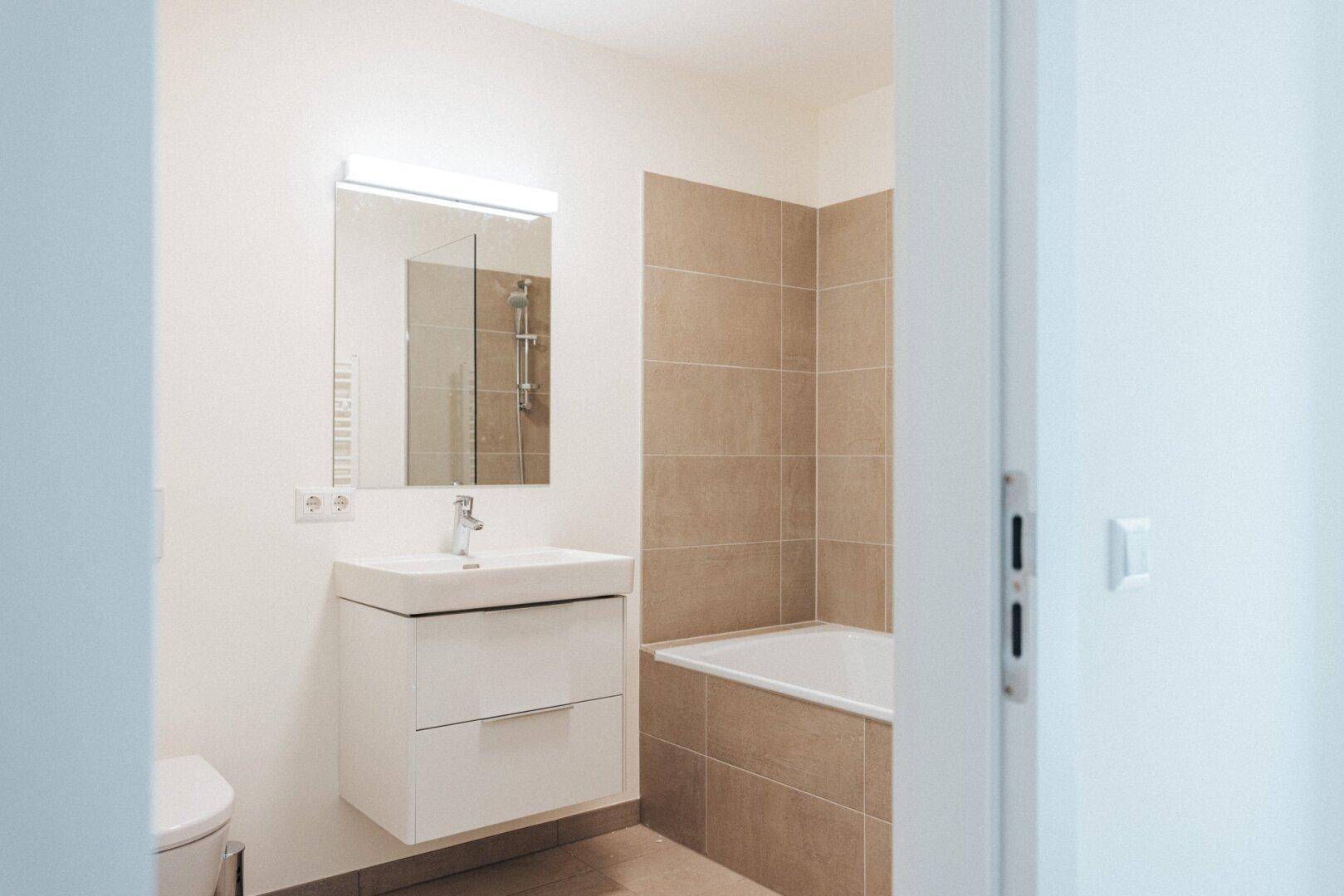 Modernes Badezimmer mit Badewanne, Einzelwaschbecken und beigefarbenen Fliesen.