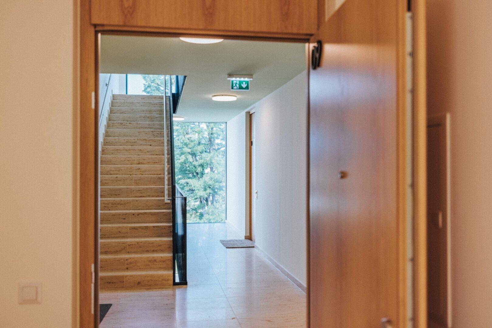 Heller Eingangsbereich mit Holztreppe und großen Fenstern, die viel Tageslicht hereinlassen.