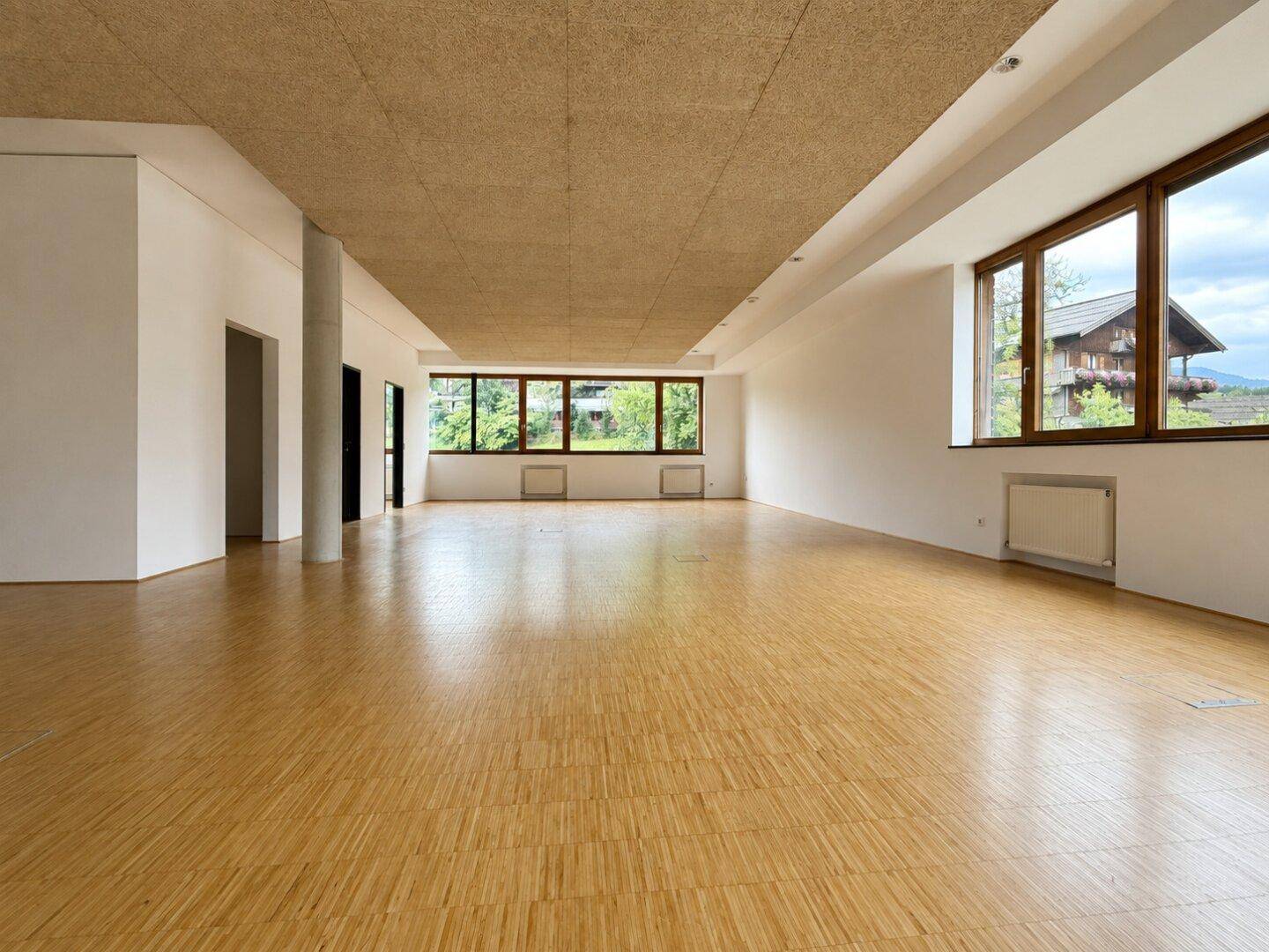 Heller Gewerberaum mit Holzboden, großen Fenstern und Blick auf die Umgebung.