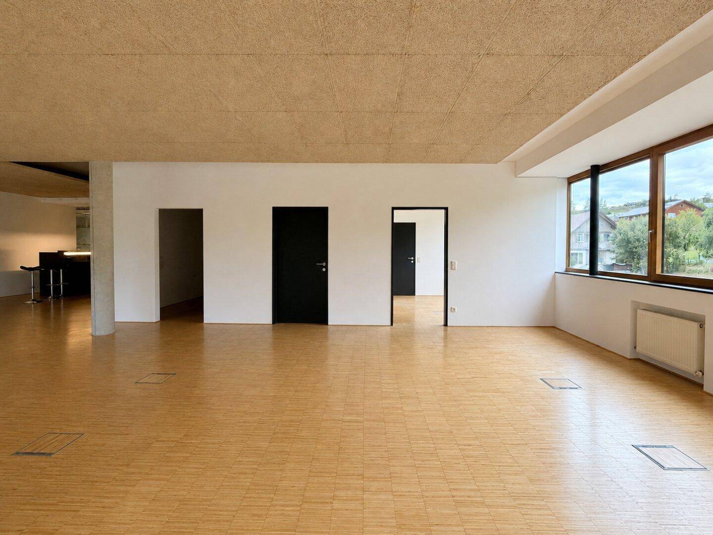 Großer, heller Gewerberaum mit Holzboden, mehreren Türen und Blick nach draußen.