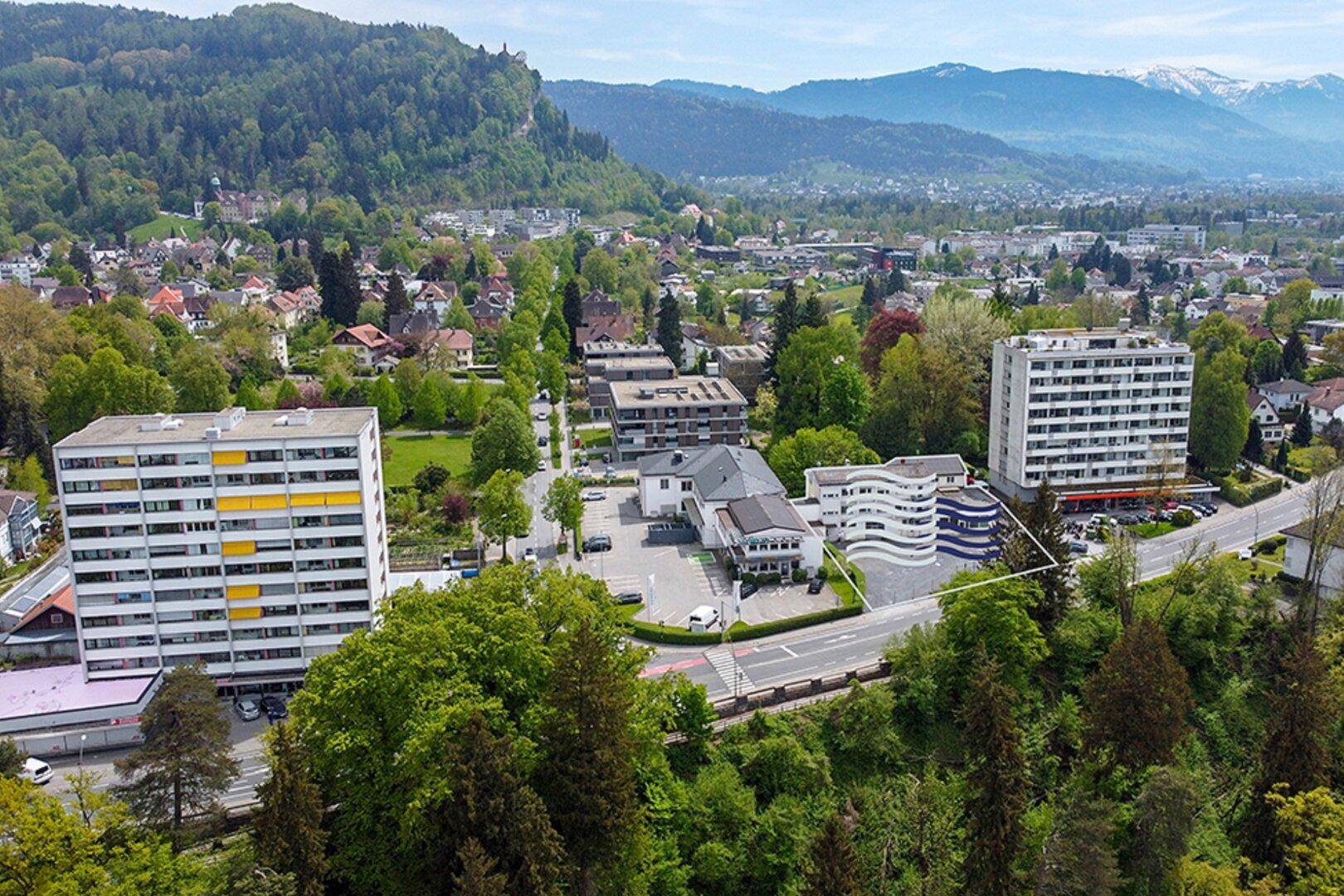 Weitläufige Luftaufnahme einer Stadt mit Bergen im Hintergrund und einer markierten Immobilie im Vordergrund.