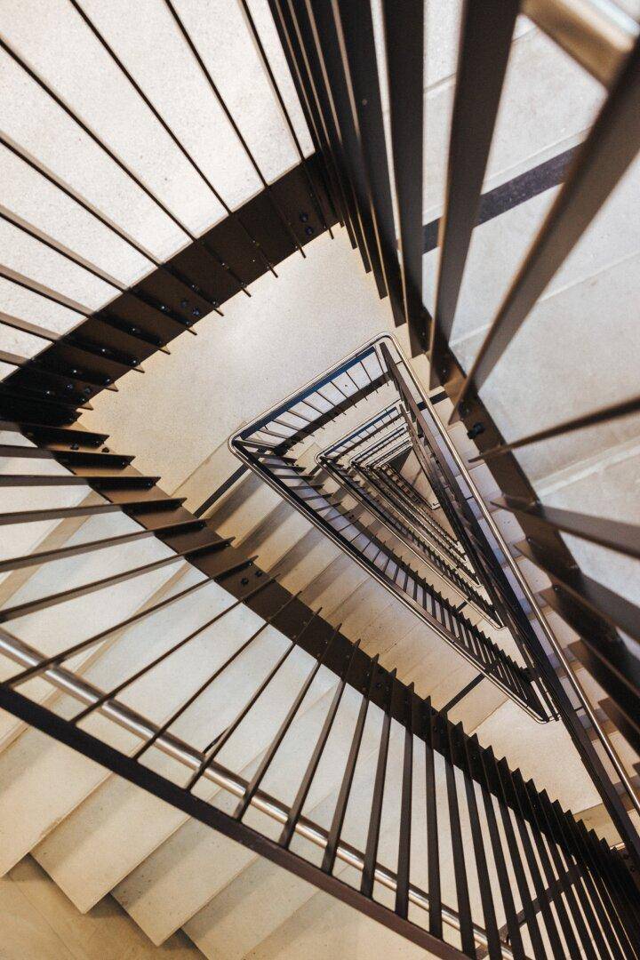 Blick von oben in ein modernes, mehrstöckiges Treppenhaus mit geometrischem Design und Metallgeländer.