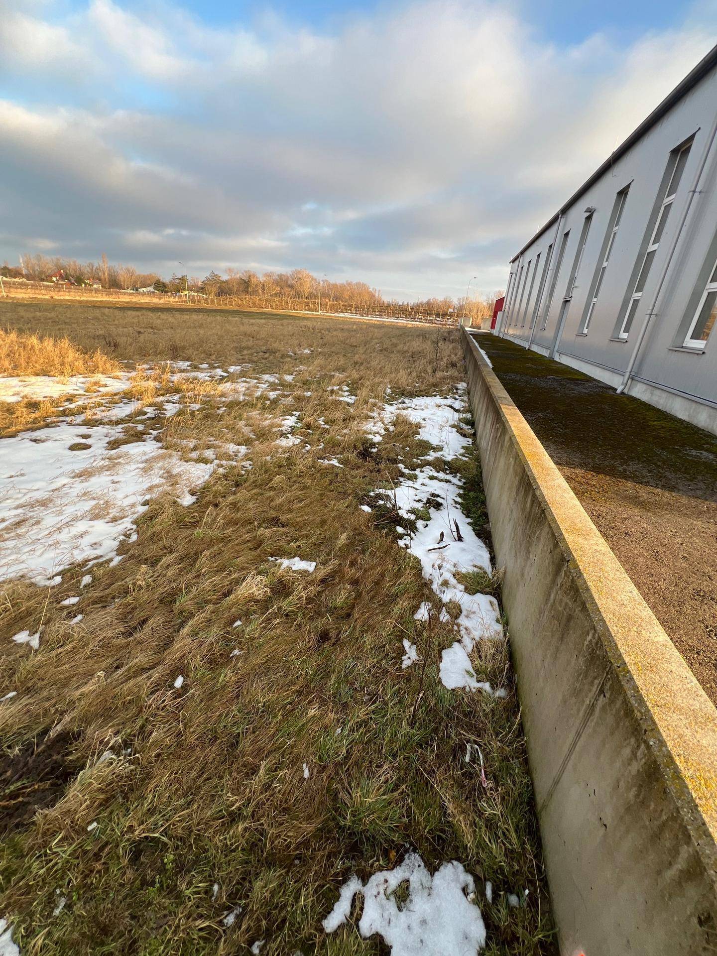 Seitenansicht eines modernen Gebäudes neben einem unbebauten Feld mit Schneeresten und weitem Blick.